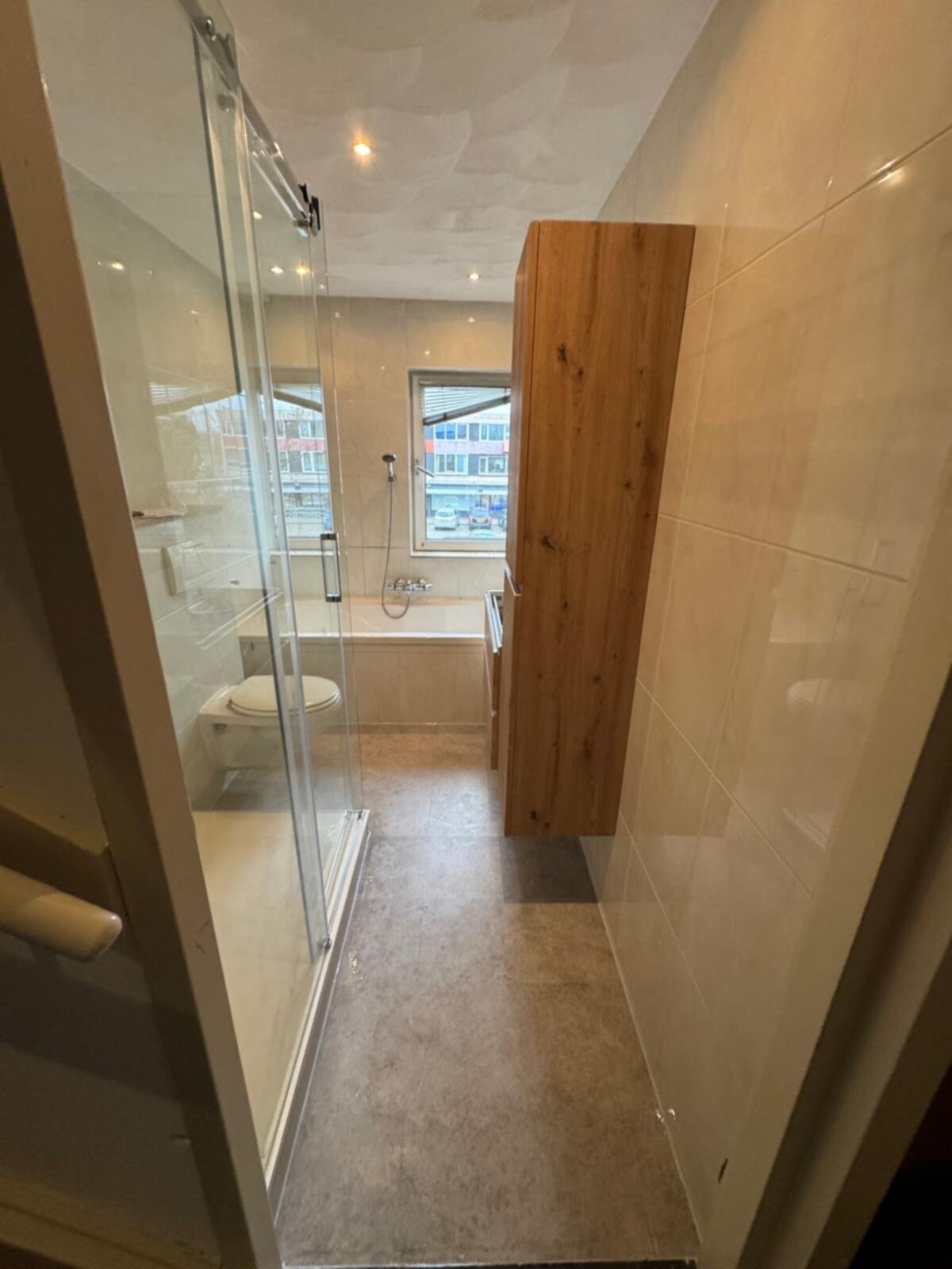 Badkamer met douche, toilet en bad, betegeld met beige tegels en houten elementen