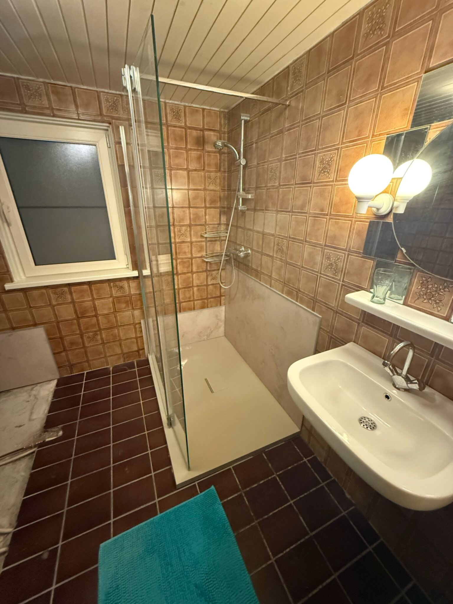 Badkamer met bruine tegels, douche, wastafel en toilet