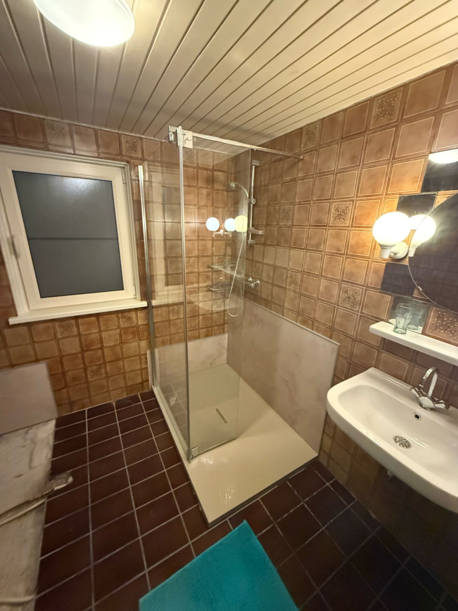 Badkamer met bruine tegels, douche, wastafel en spiegel
