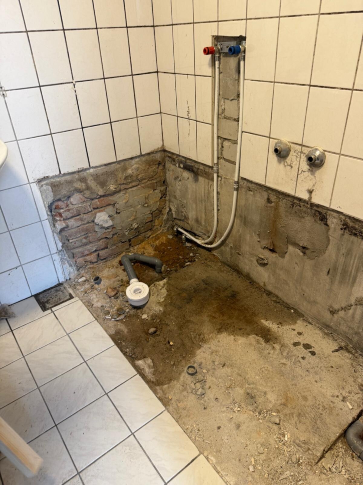 Slechte staat badkamer met kapotte tegelwand en open leidingen