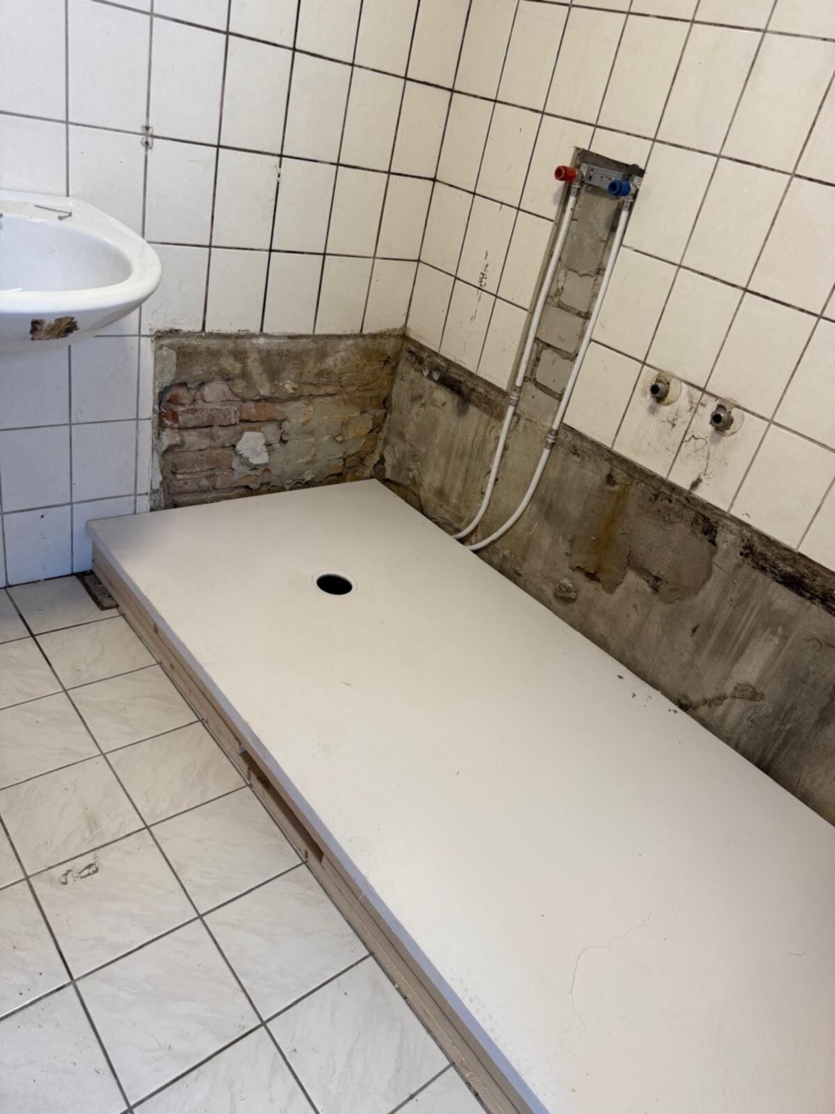 Badkamer in renovatie, betegelde muren en vloer, oude douchebasis en wastafel