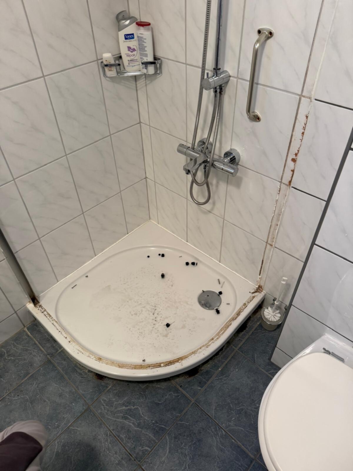Vieze, oude douchebak met betegelde muren en verouderde accessoires