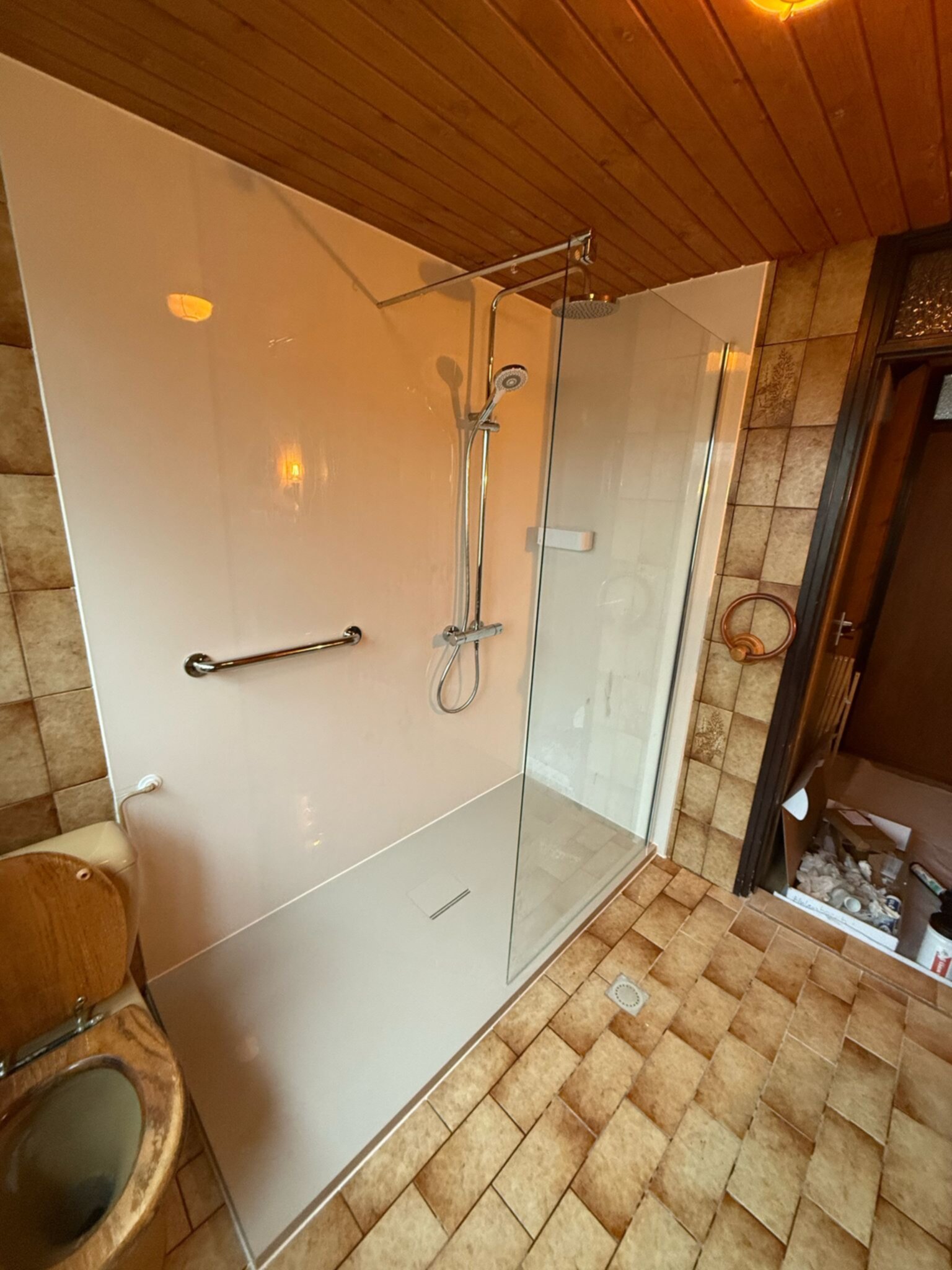 Badkamer met douche, toilet en bruine tegelvloer en -wanden
