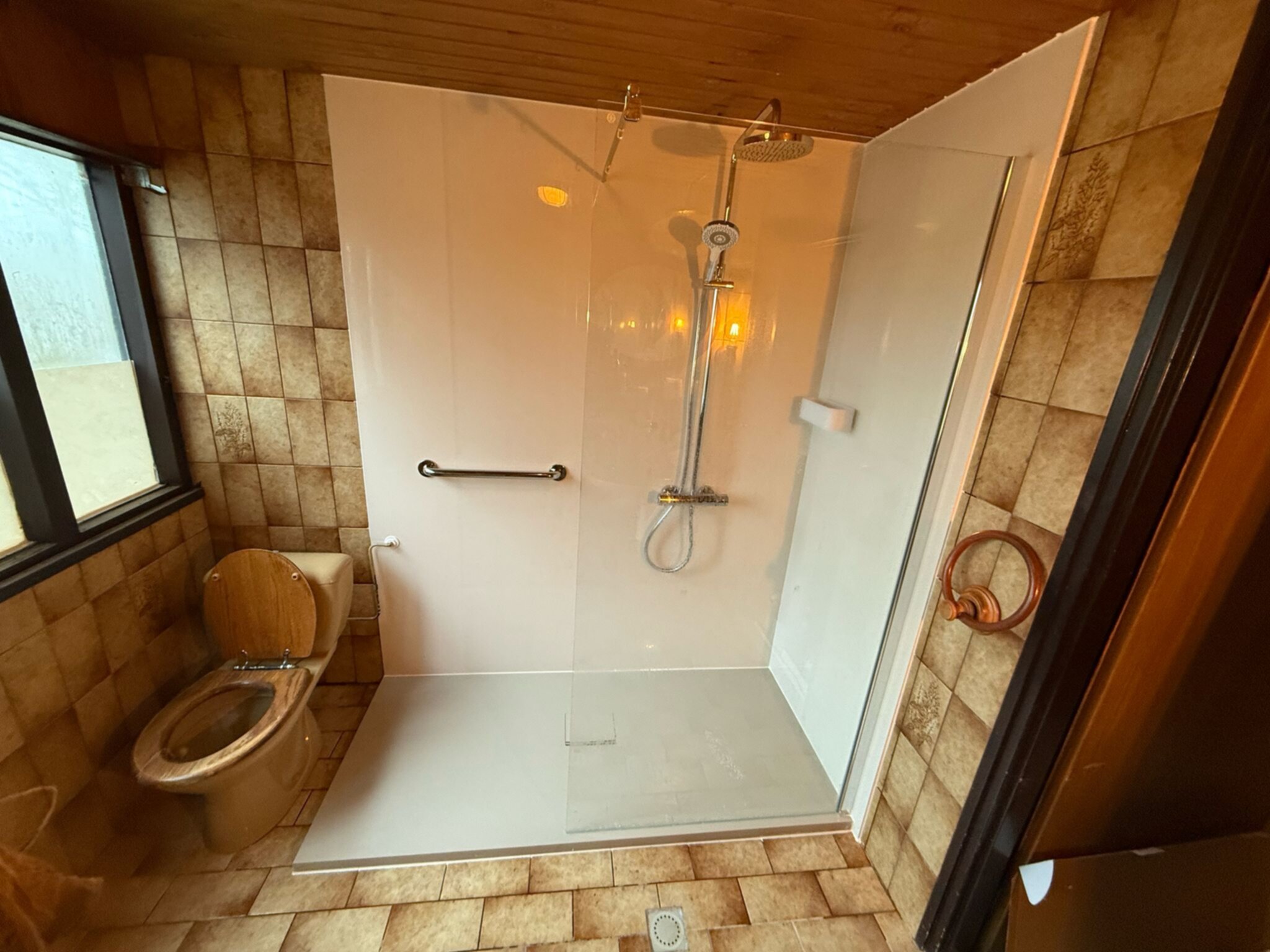 Badkamer met beige betegelde muren en vloer, toilet en douche met glazen deur
