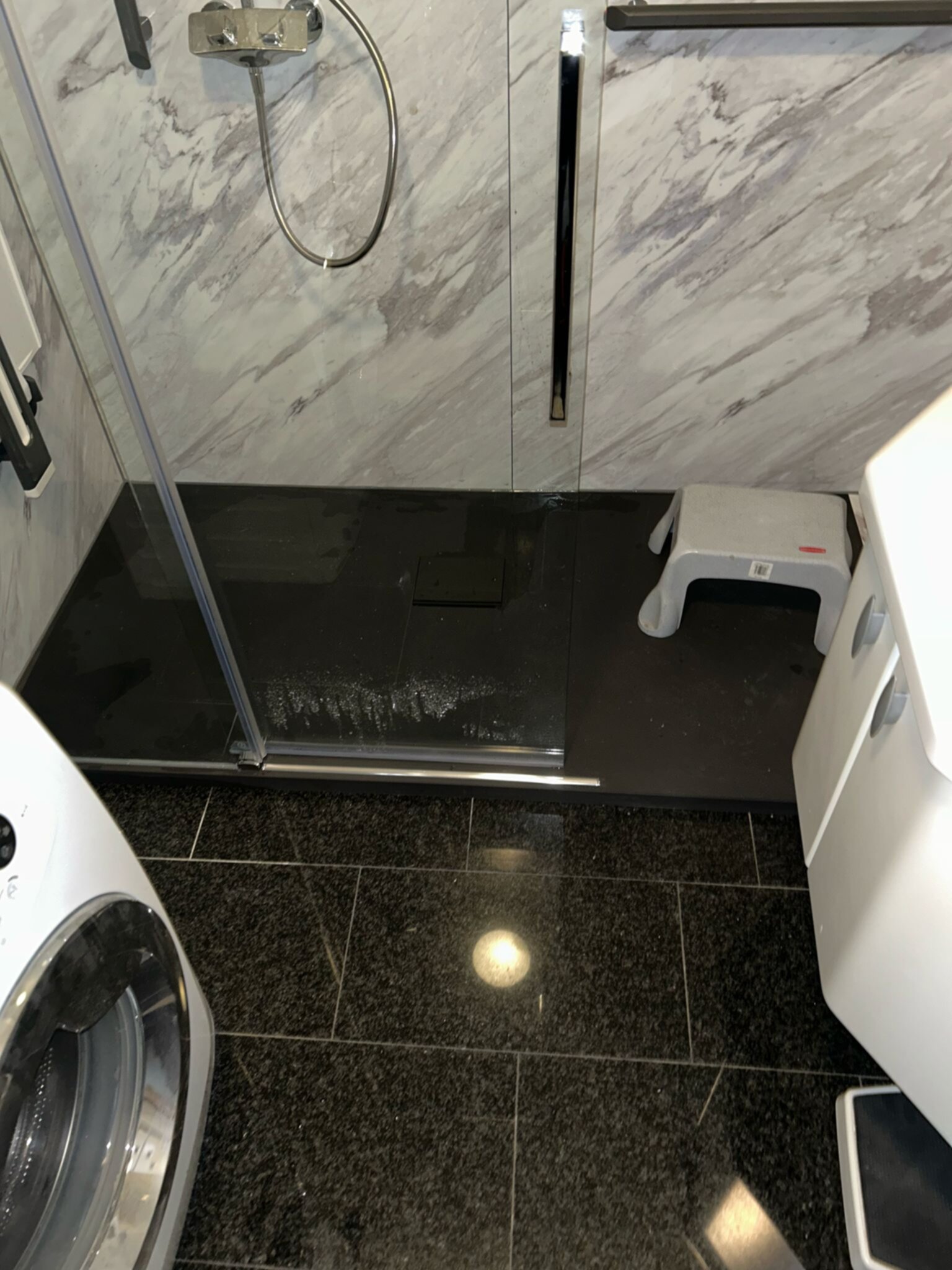 Douchevloer met zwarte tegel en marmerlook wanden, wasmachine en toilet zichtbaar