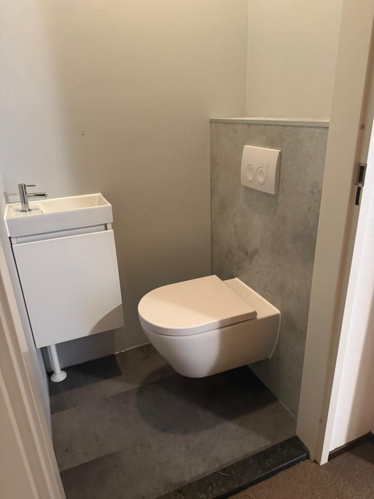 Wit toilet en wastafel in kleine badkamer met grijze betonlook vloer en wand