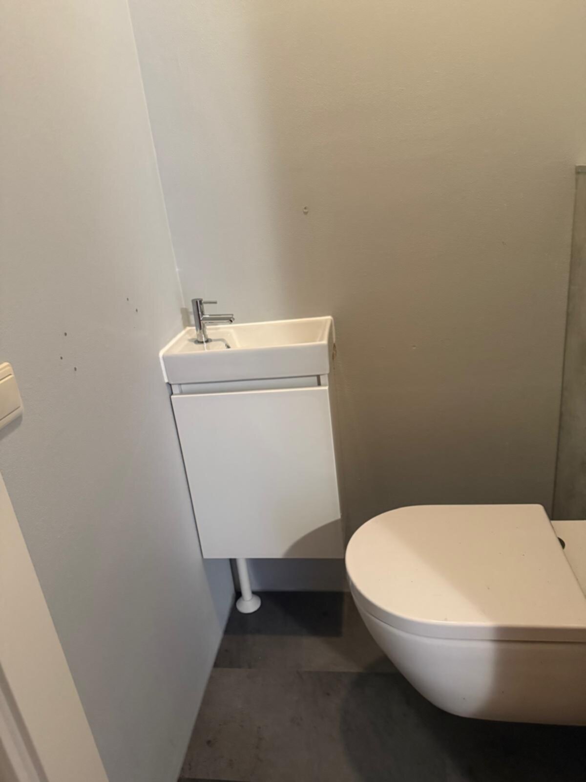 Wit betegelde badkamer met toilet en wastafel