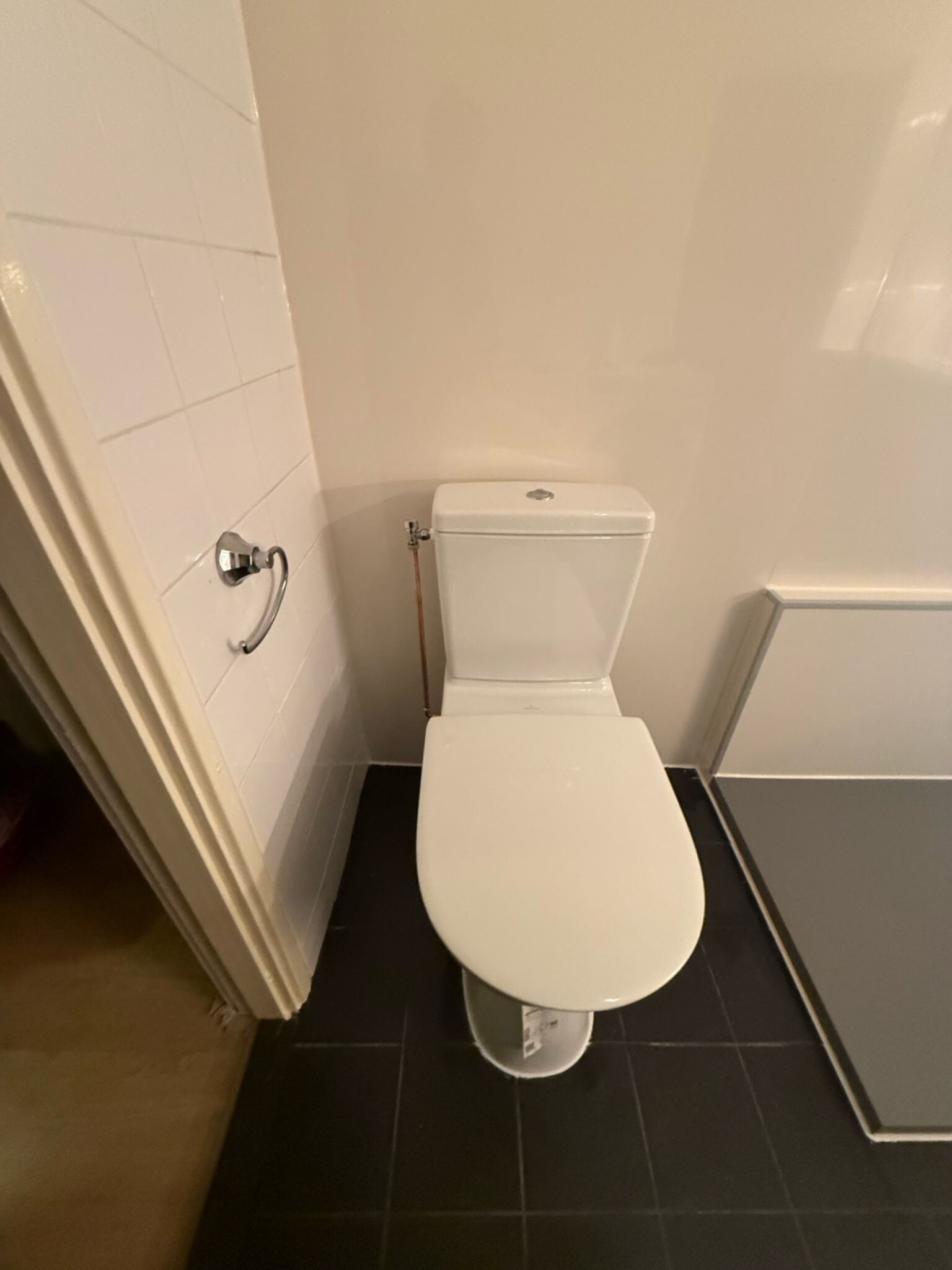 Wit toilet in badkamer met witte tegelwand en zwarte vloer