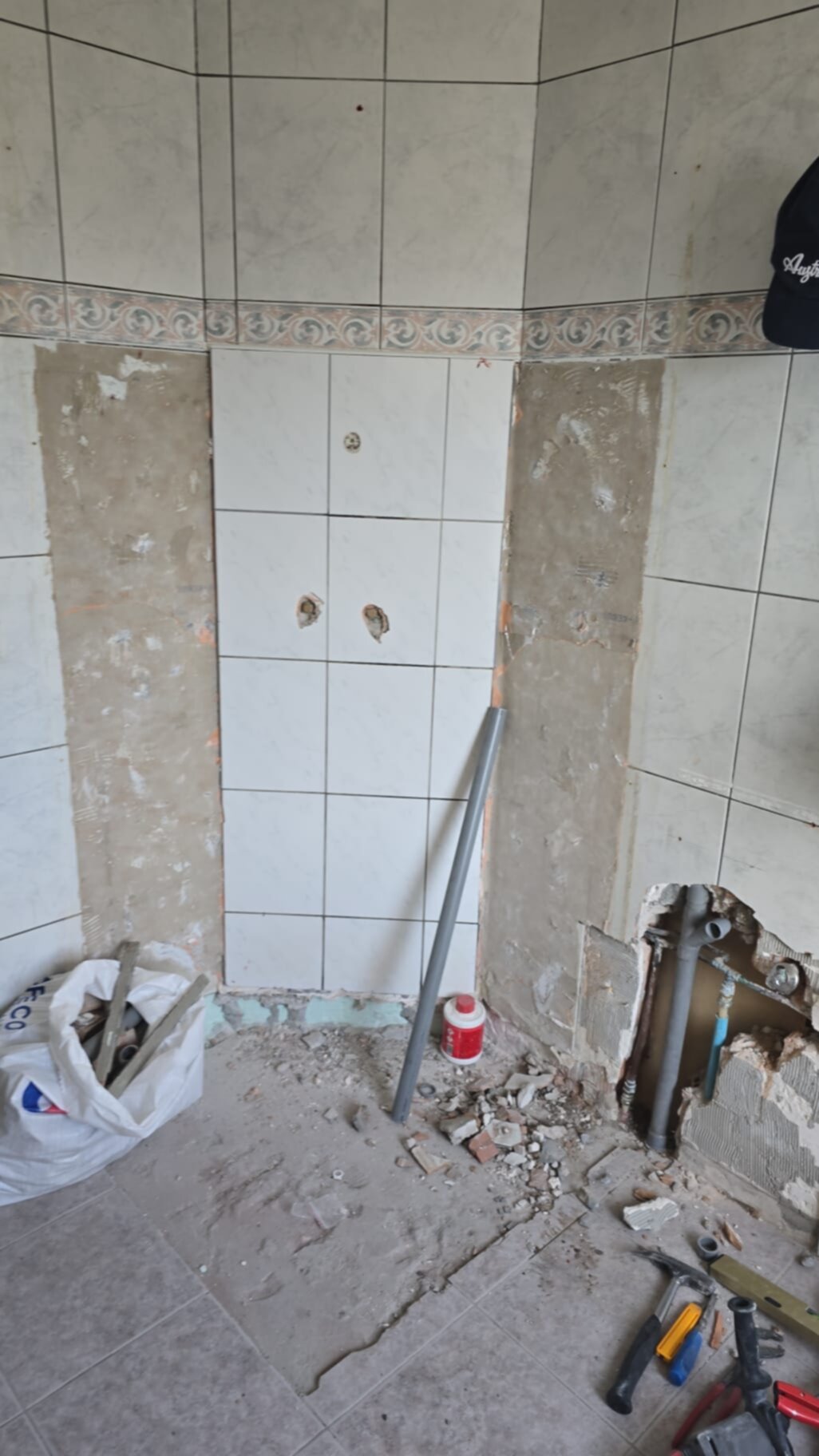 Slechte badkamer in renovatie, grijs en wit betegeld met bouwmaterialen en gereedschap