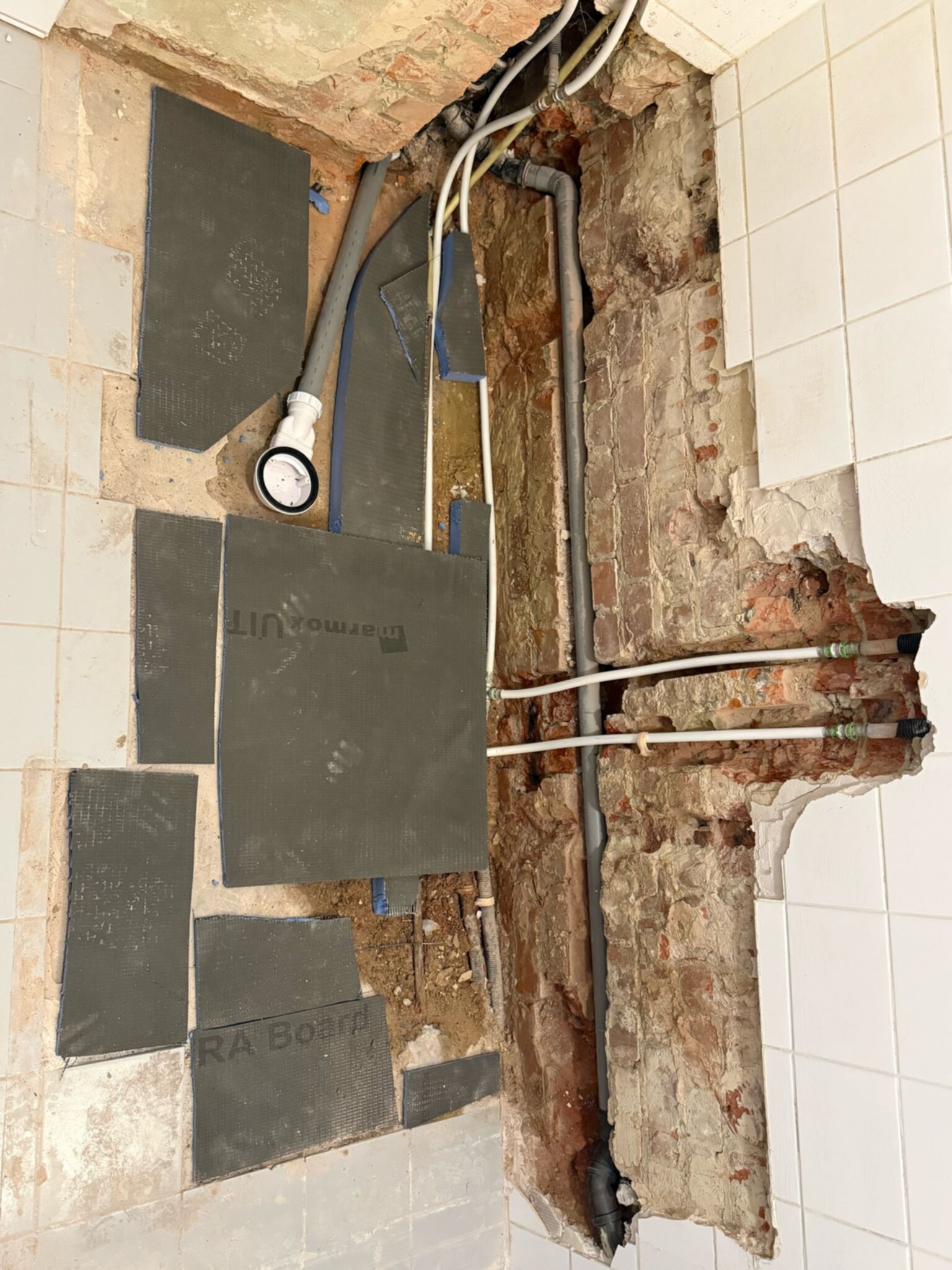 Badkamer renovatie tijdens werkzaamheden, zicht op de betegelde vloer en opengelegde leidingen
