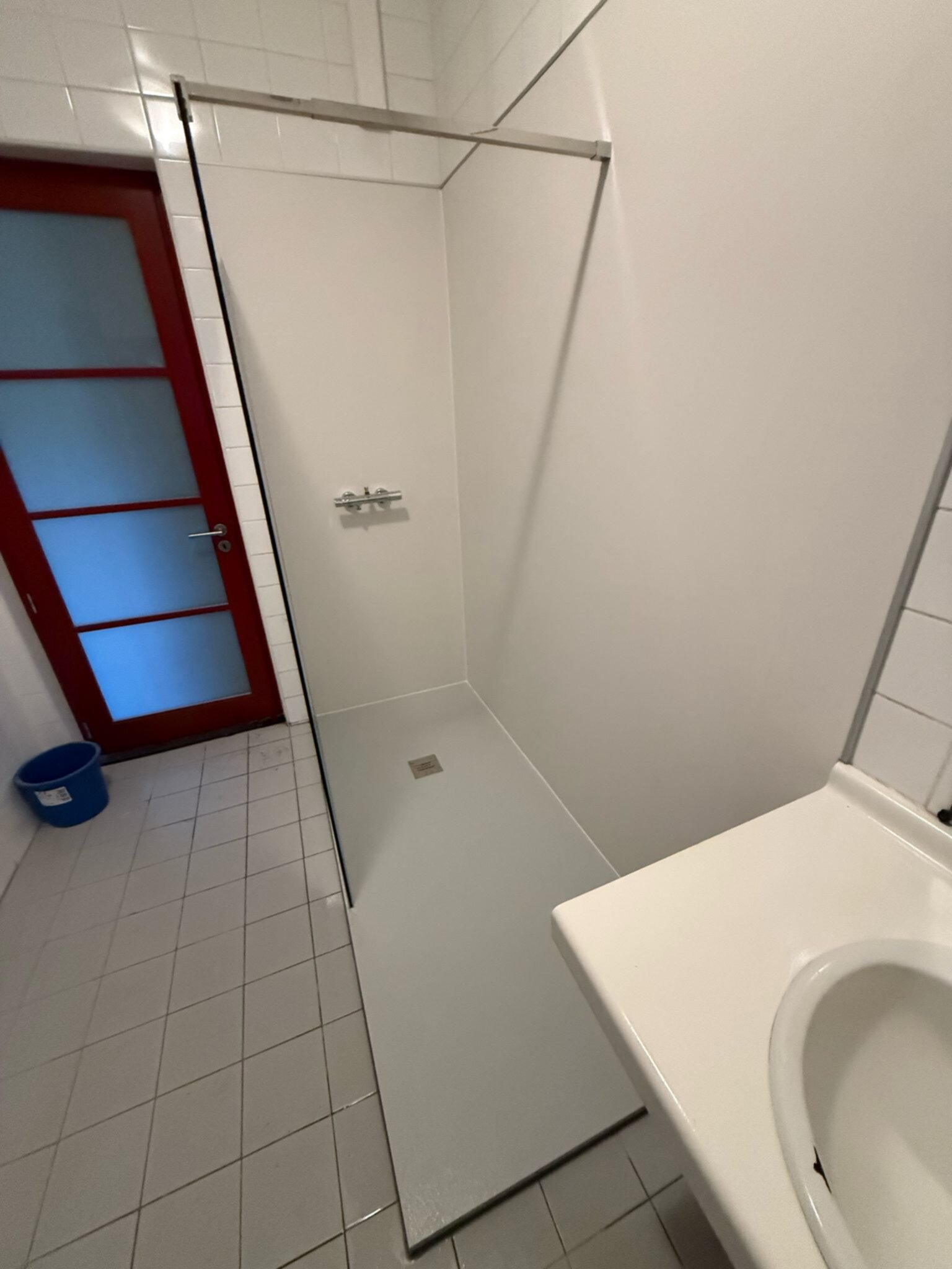 Wit betegelde badkamer met glazen douchewand en witte wasbak