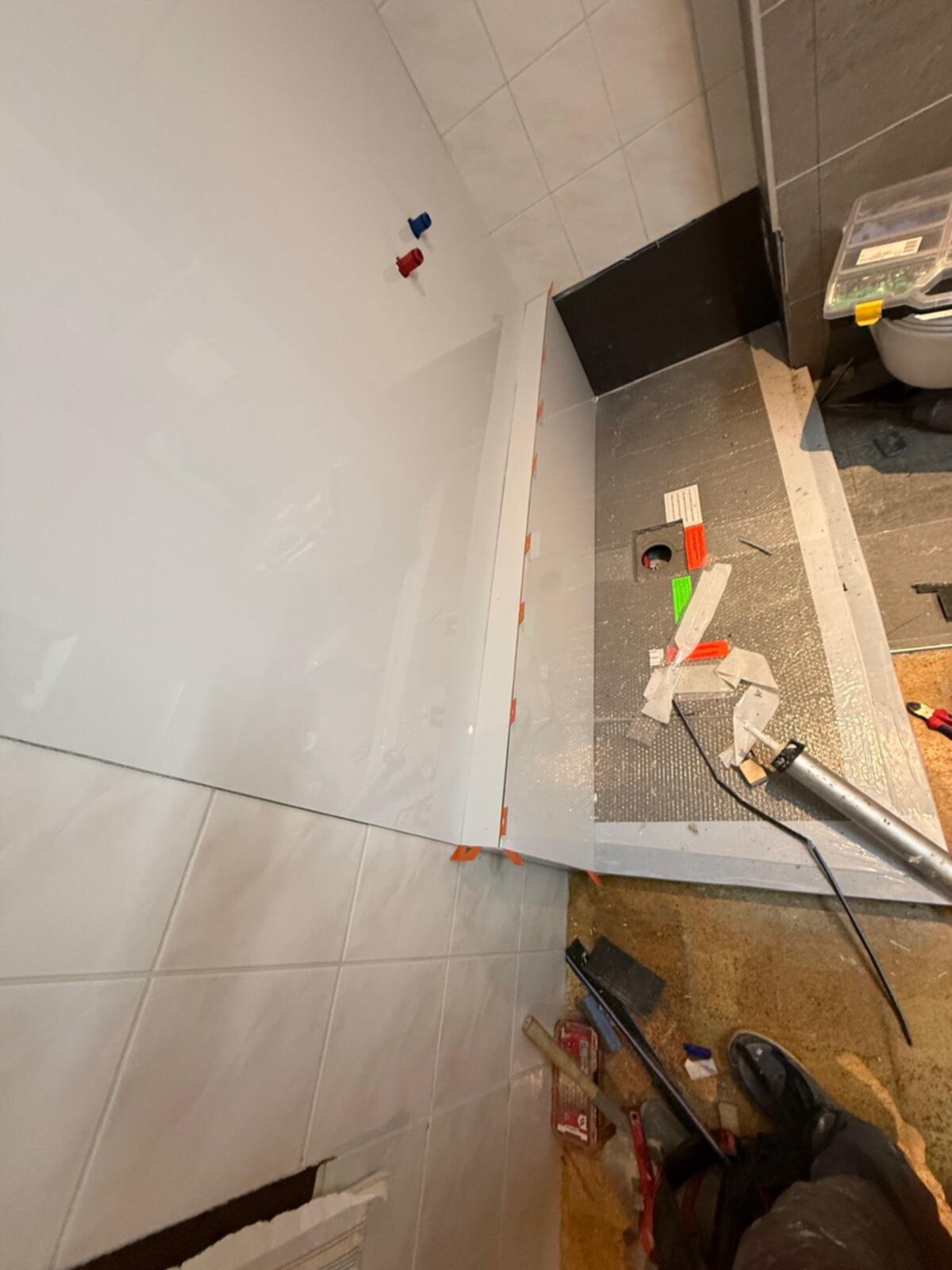 Wit betegelde badkamerhoek met gereedschap en materialen tijdens renovatie