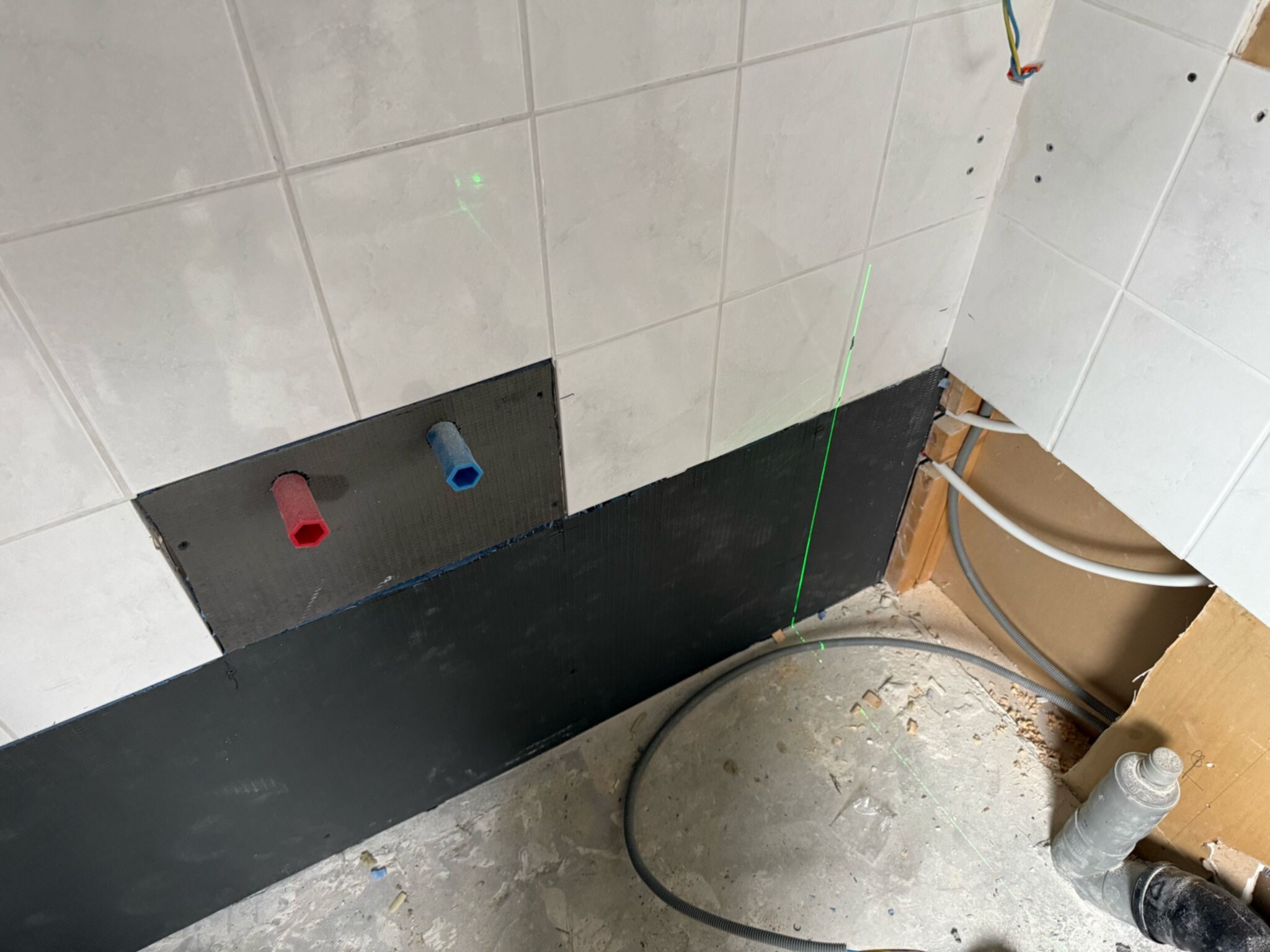 Wit betegelde badkamer wand met rode en blauwe waterleidingen en bouwmaterialen