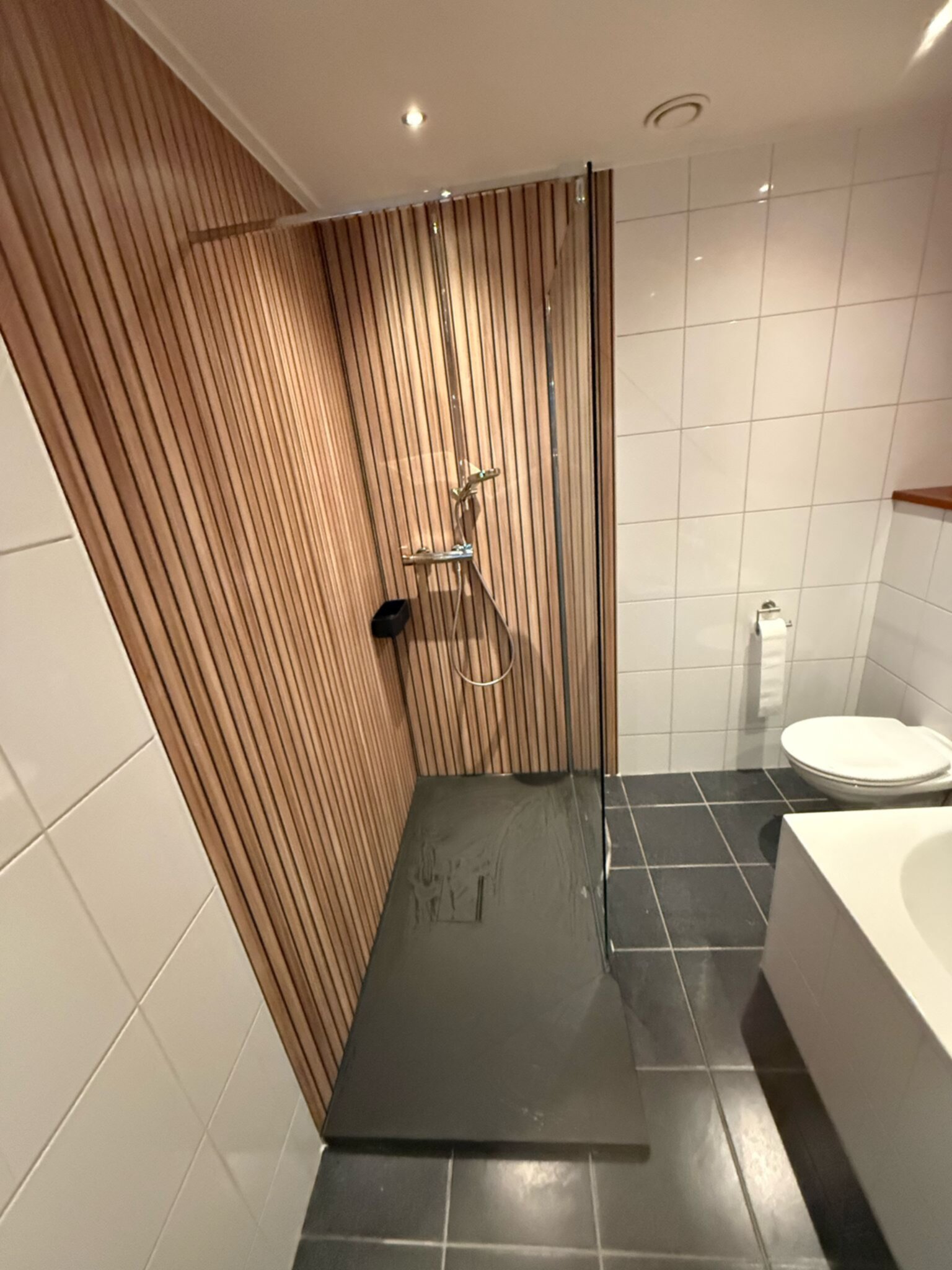 Badkamer met houten wandpanelen, witte tegels en donkere vloer