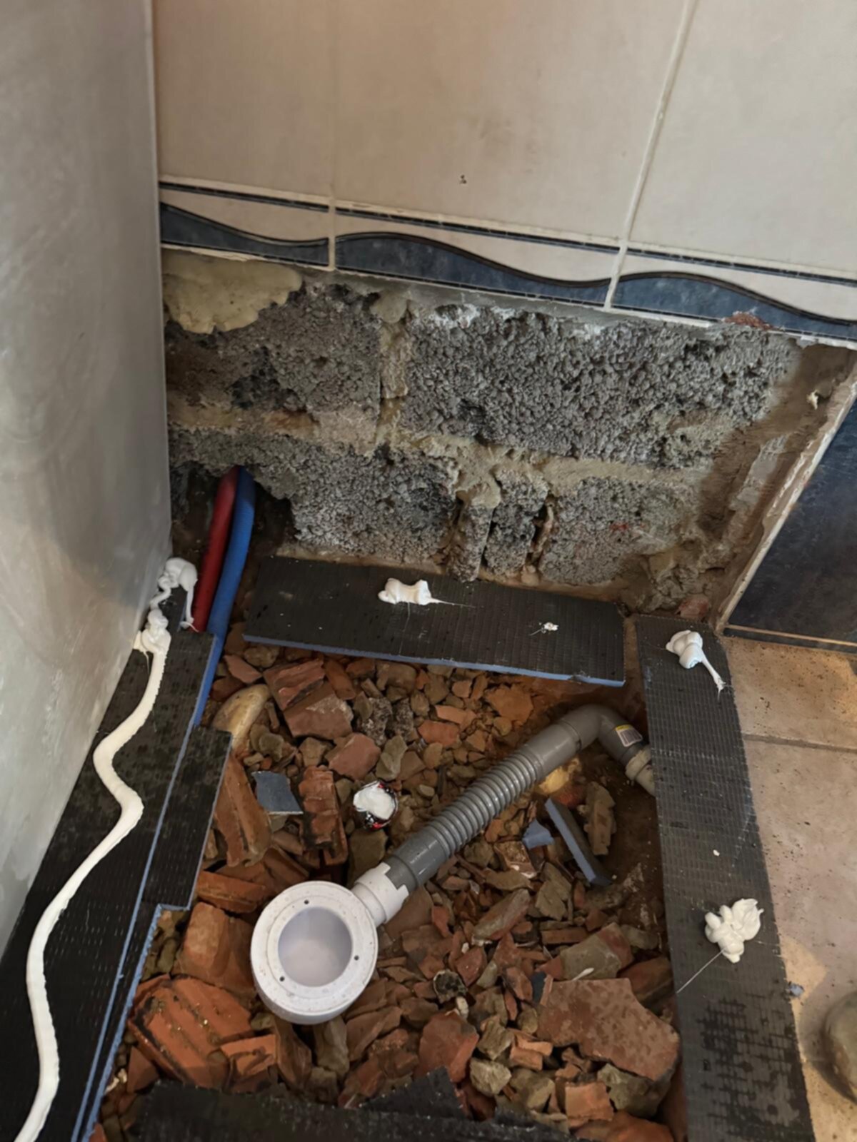 Slecht onderhouden badkamer met open liggende leidingen en beschadigde tegelwerk