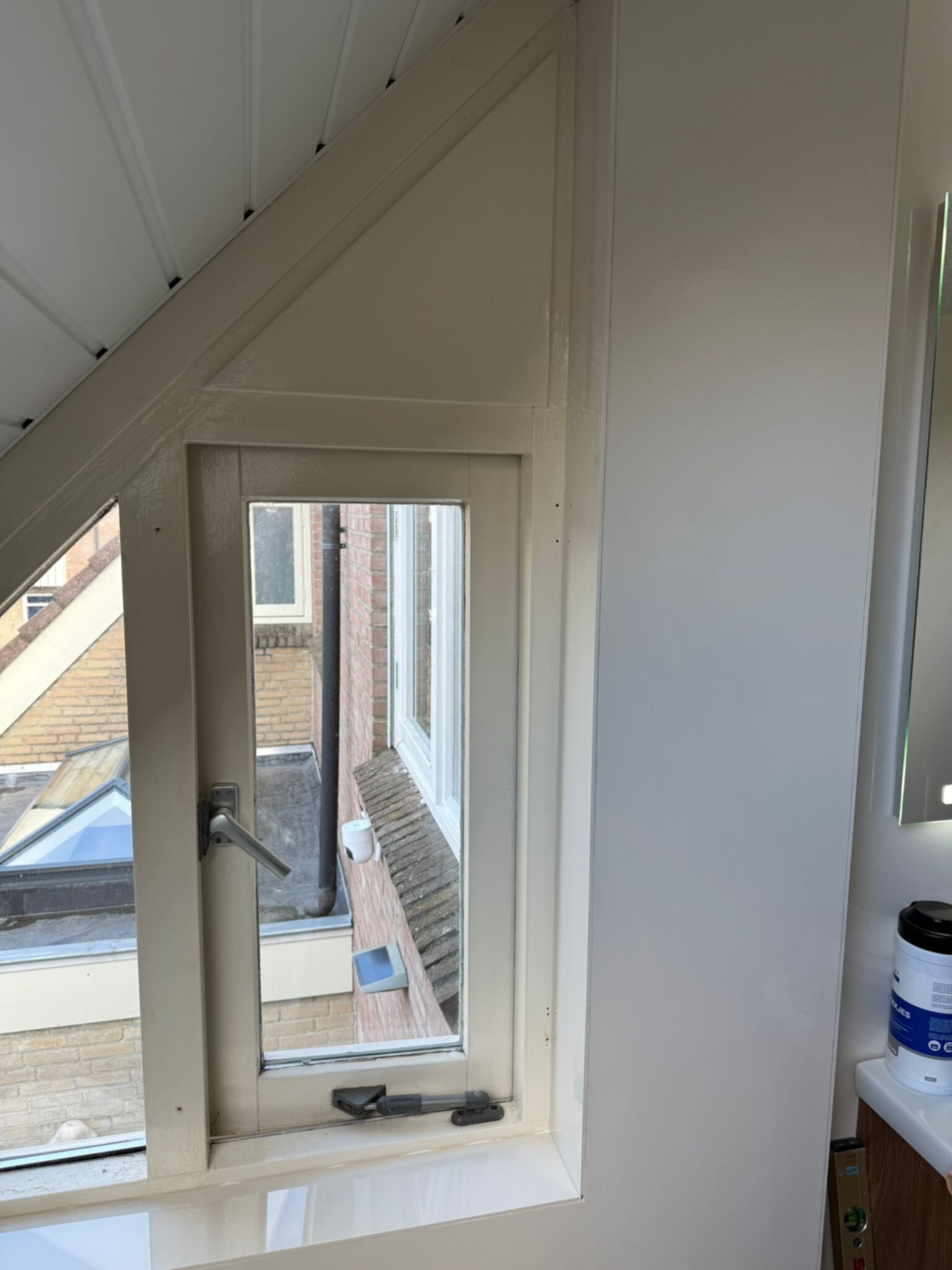 Schuin dakraam in witte badkamer met uitzicht op dak en bakstenen muur