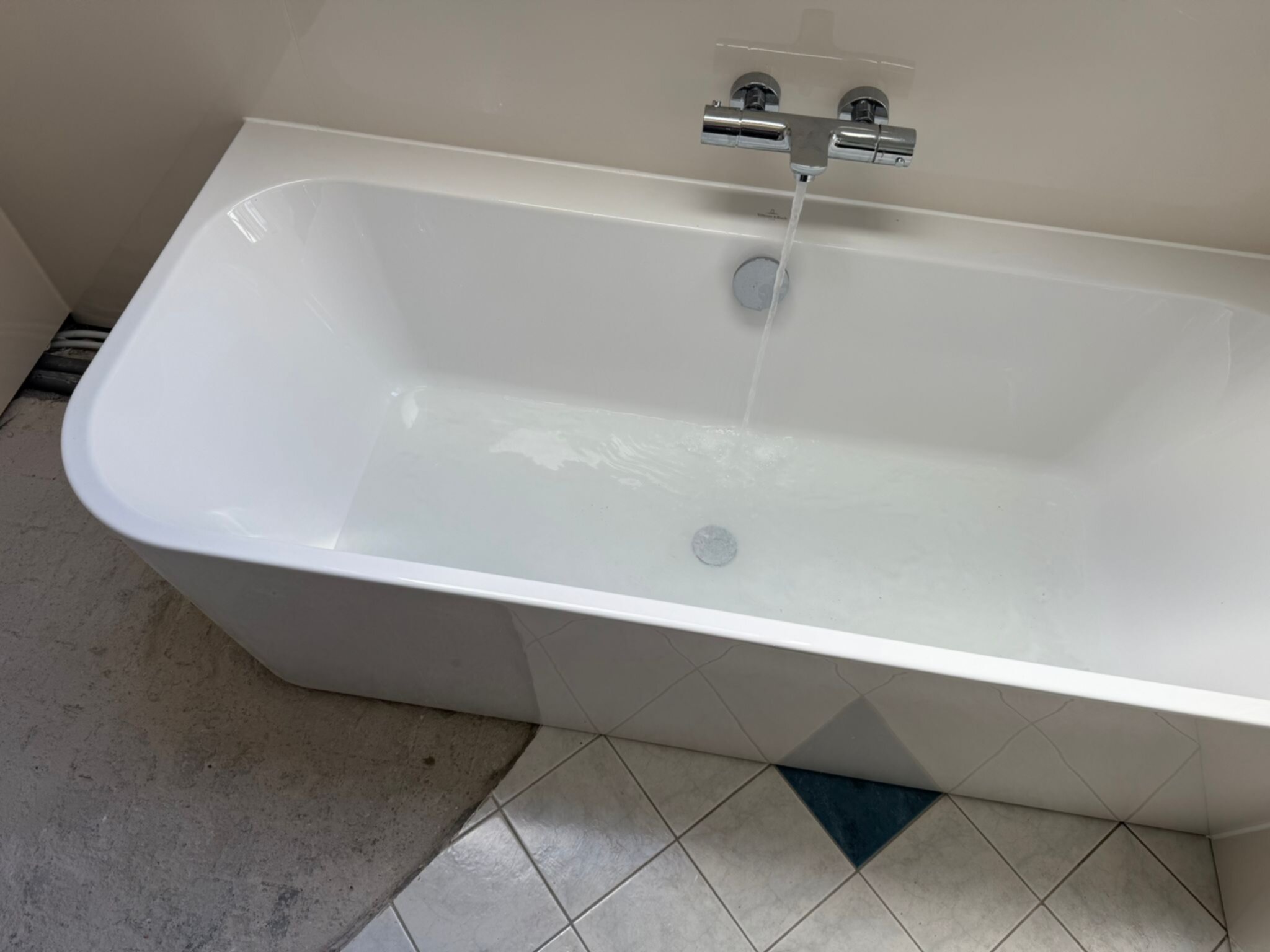 Wit bad met chroom kraan en water in een betegelde badkamer