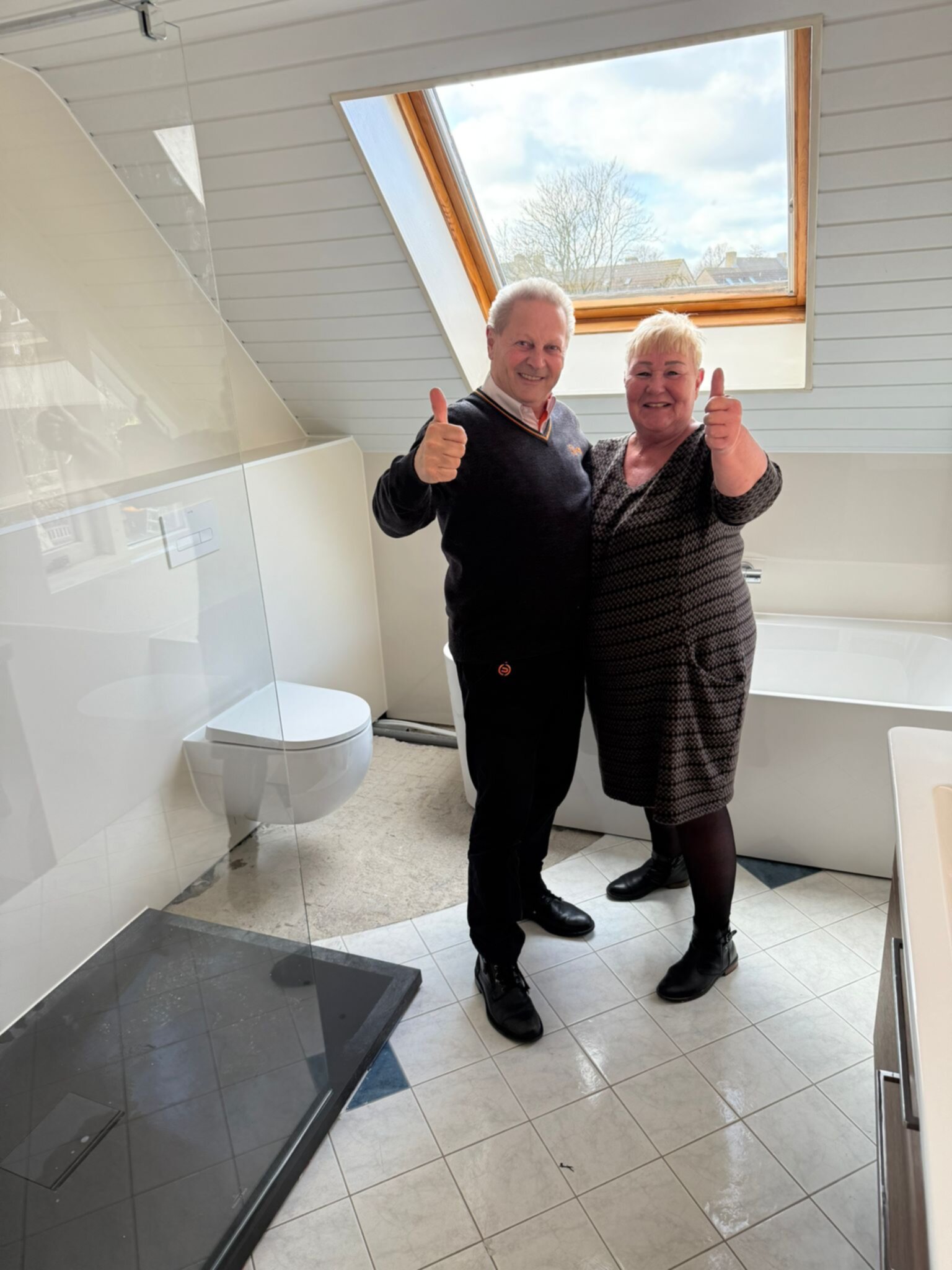 Twee tevreden klanten in hun nieuwe badkamer met dakkapel en witte betegeling