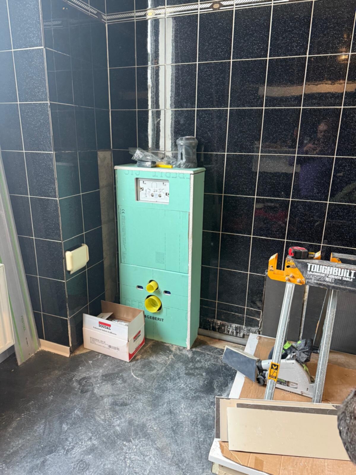 Tijdens badkamer renovatie, groene installatiekast en zwarte tegels