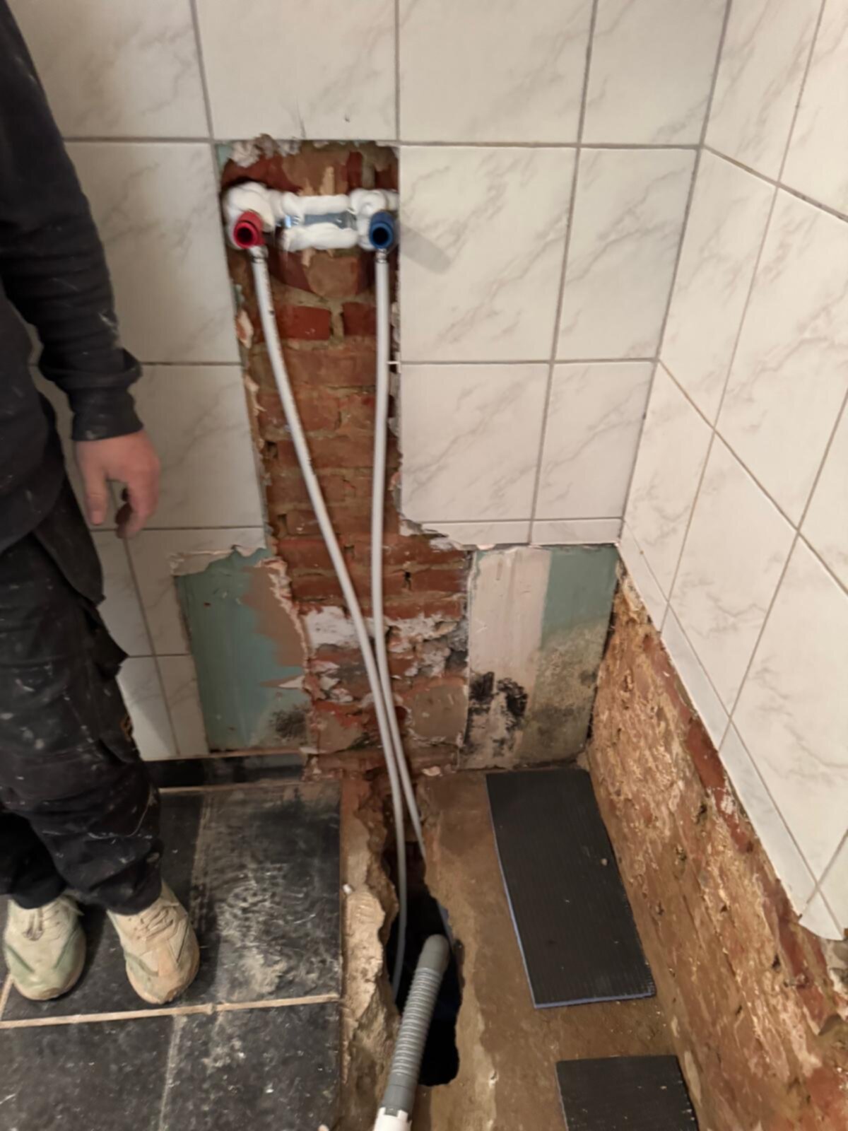 Sloopwerk badkamer met zicht op de waterleidingen en betegelde wand