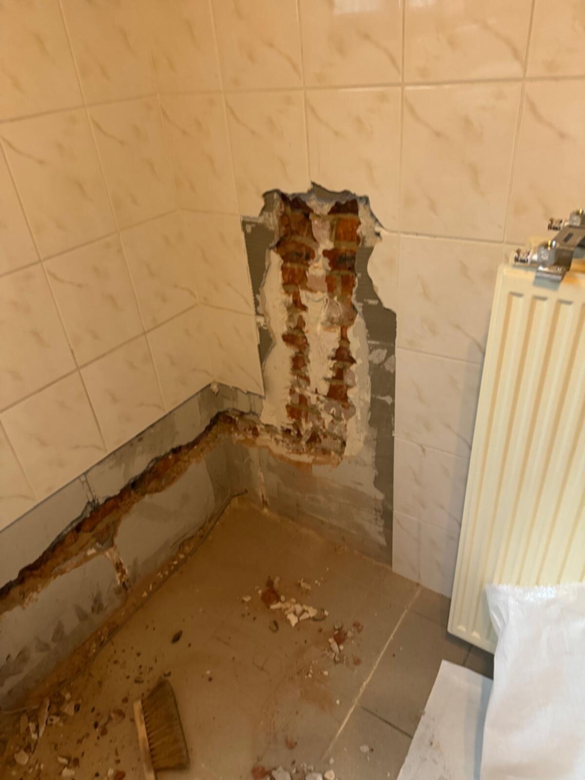 Gat in de badkamerwand met zicht op rode stenen en grijze specie