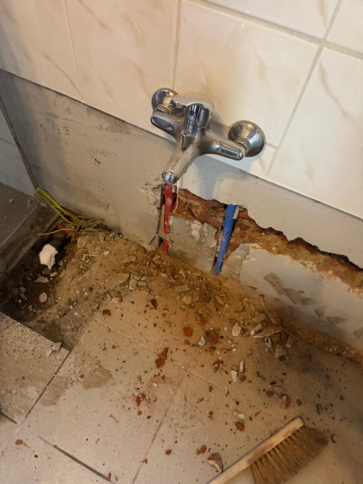 Sleuf in badkamerwand met blootgelegde leidingen en kraan