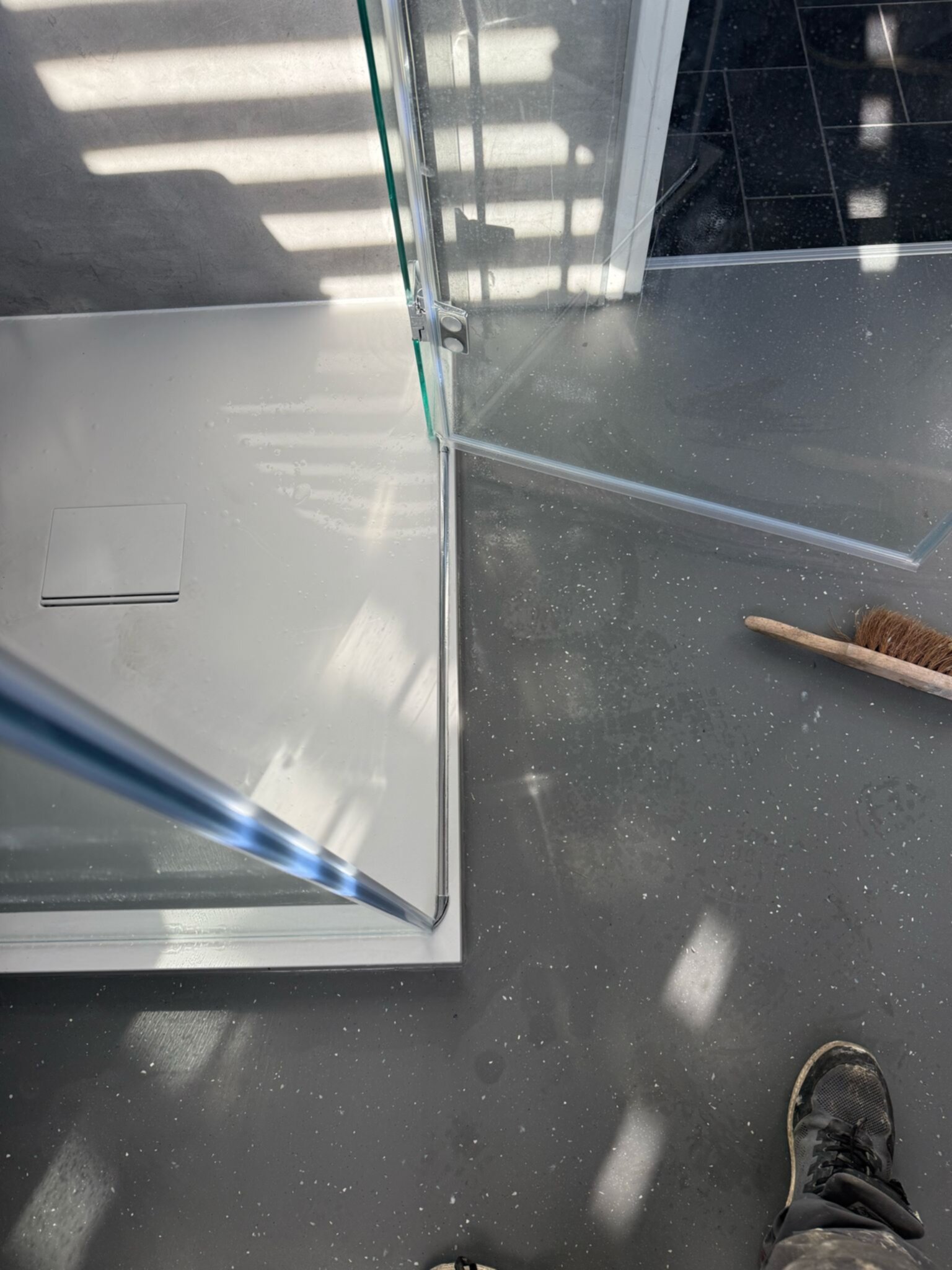 Douchehoek met glazen wand en grijs betegelde vloer tijdens renovatie
