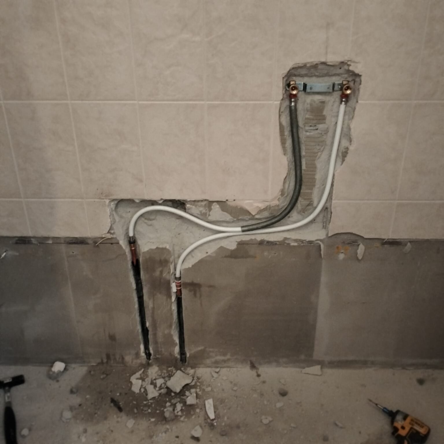 Sleuf in badkamerwand met blootgelegde waterleidingen en elektriciteitskabels