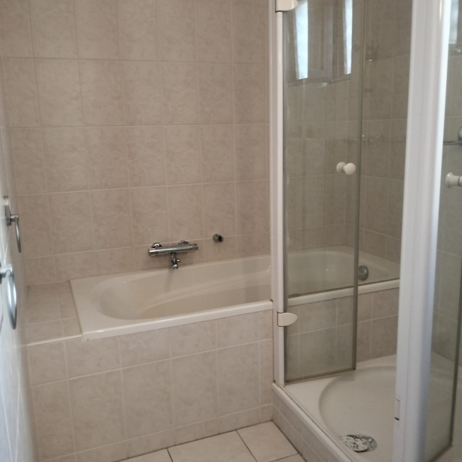 Badkamer met beige tegels, bad en douche met glazen deur