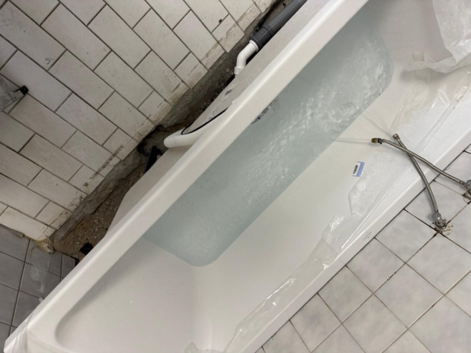 Wit bad met plastic beschermingslaag, waterleidingen en betegelde muren en vloer