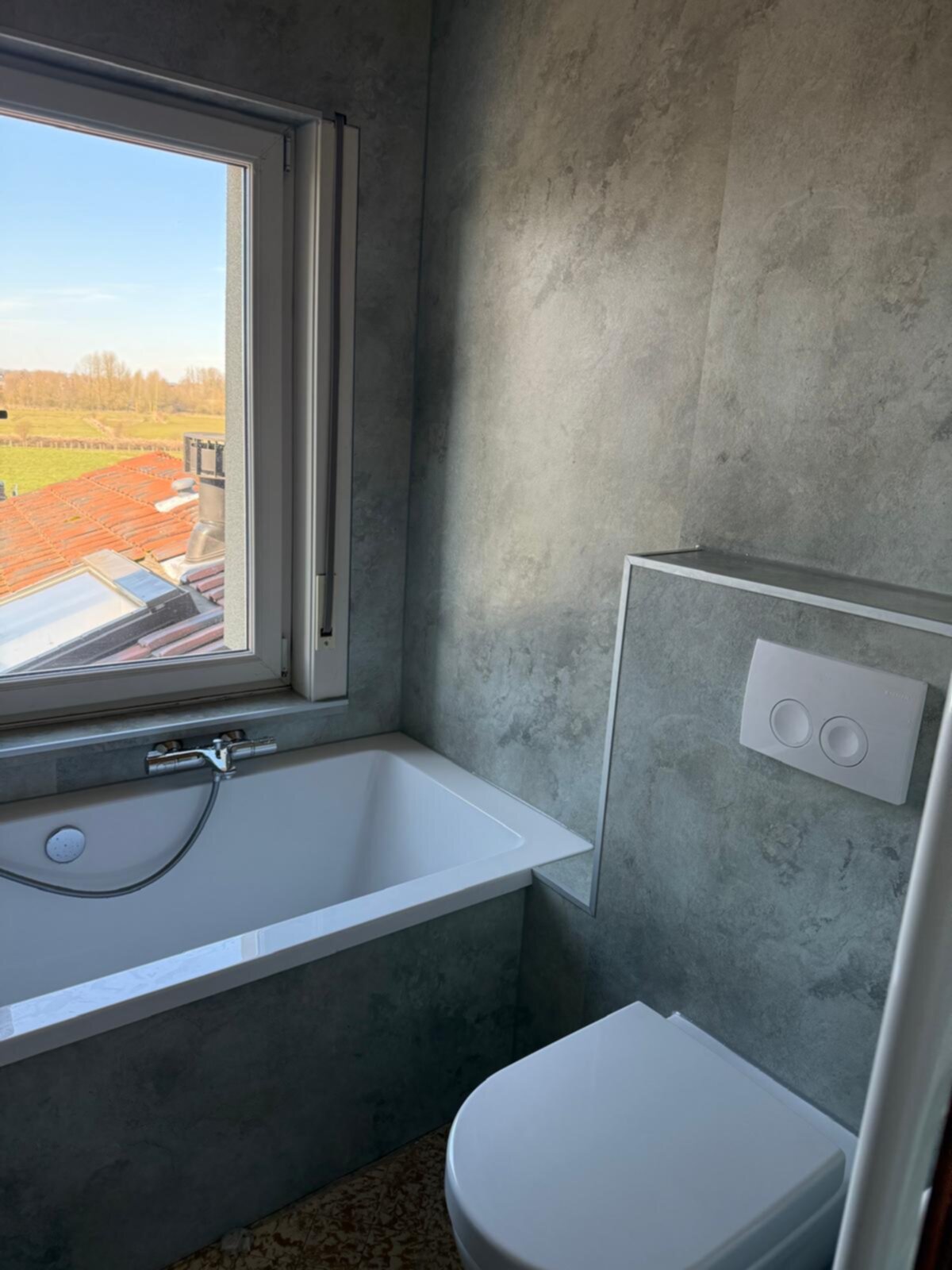 Wit bad en toilet met grijze betonlook wanden en uitzicht op het dak