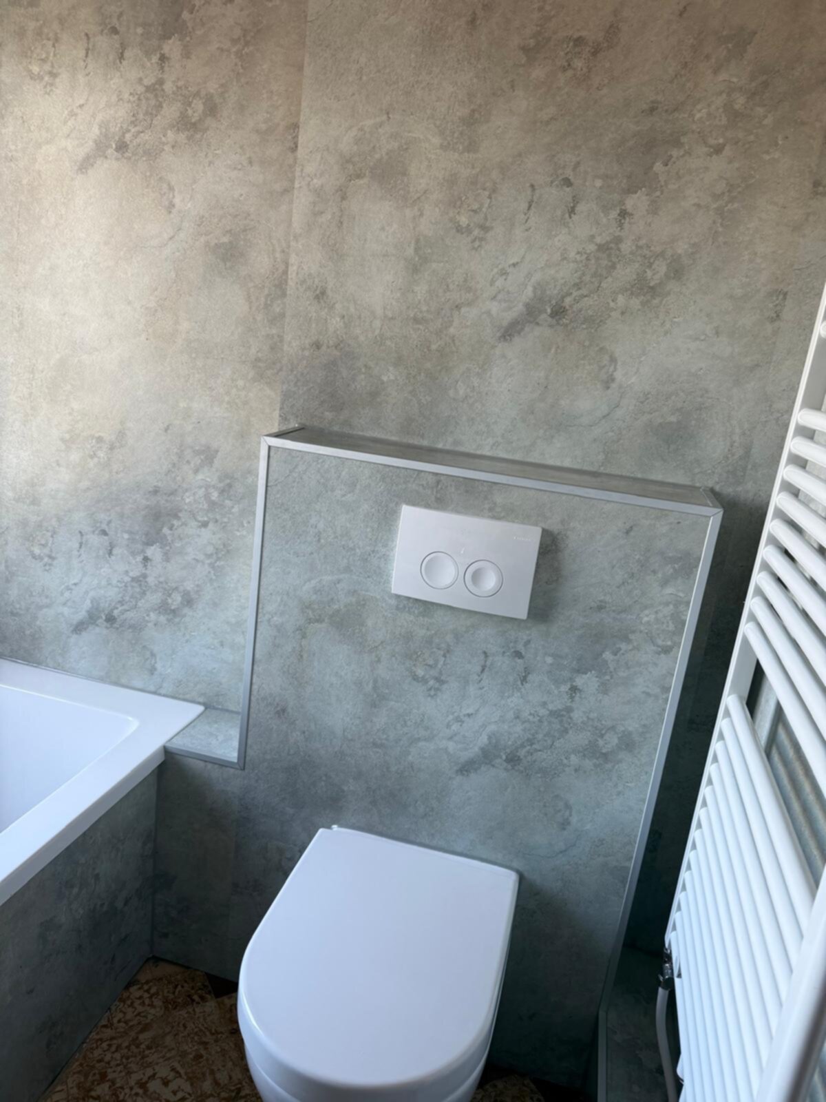 Wit toilet en badkuip tegen grijze betonnen wand met betegelde uitbouw