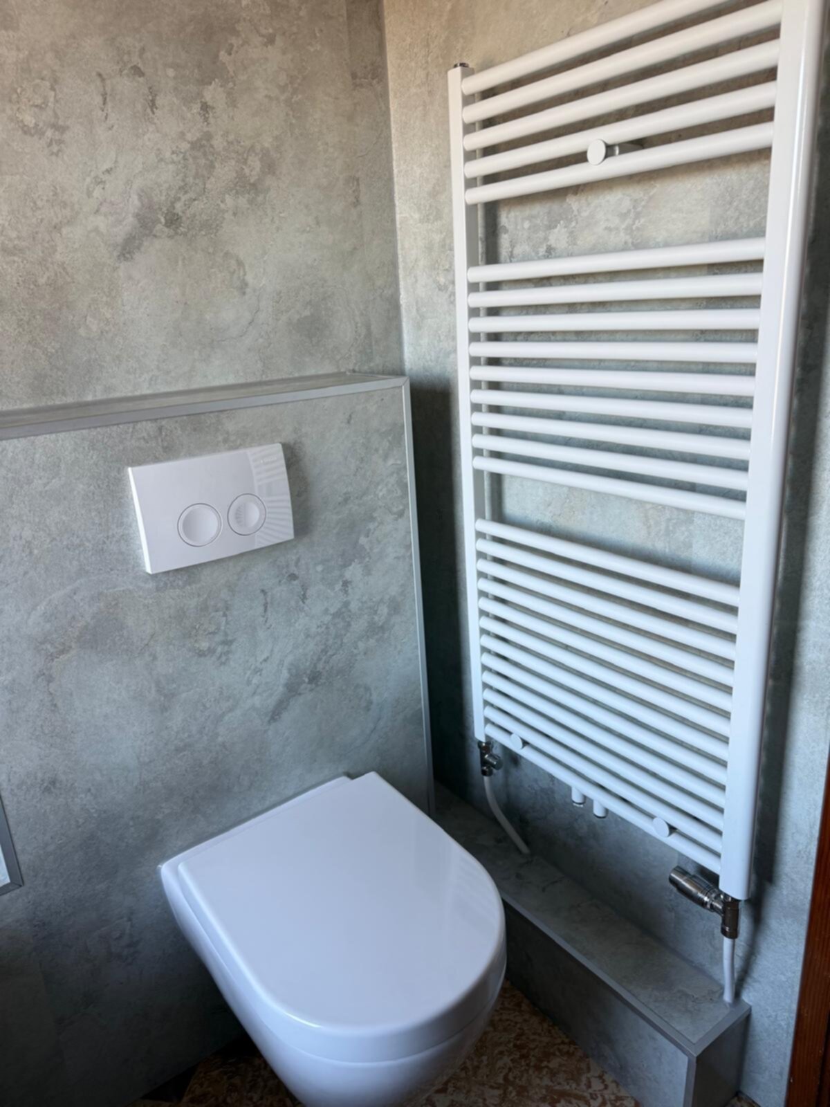 Wit toilet en verwarmde handdoek radiator in grijze betegelde badkamer