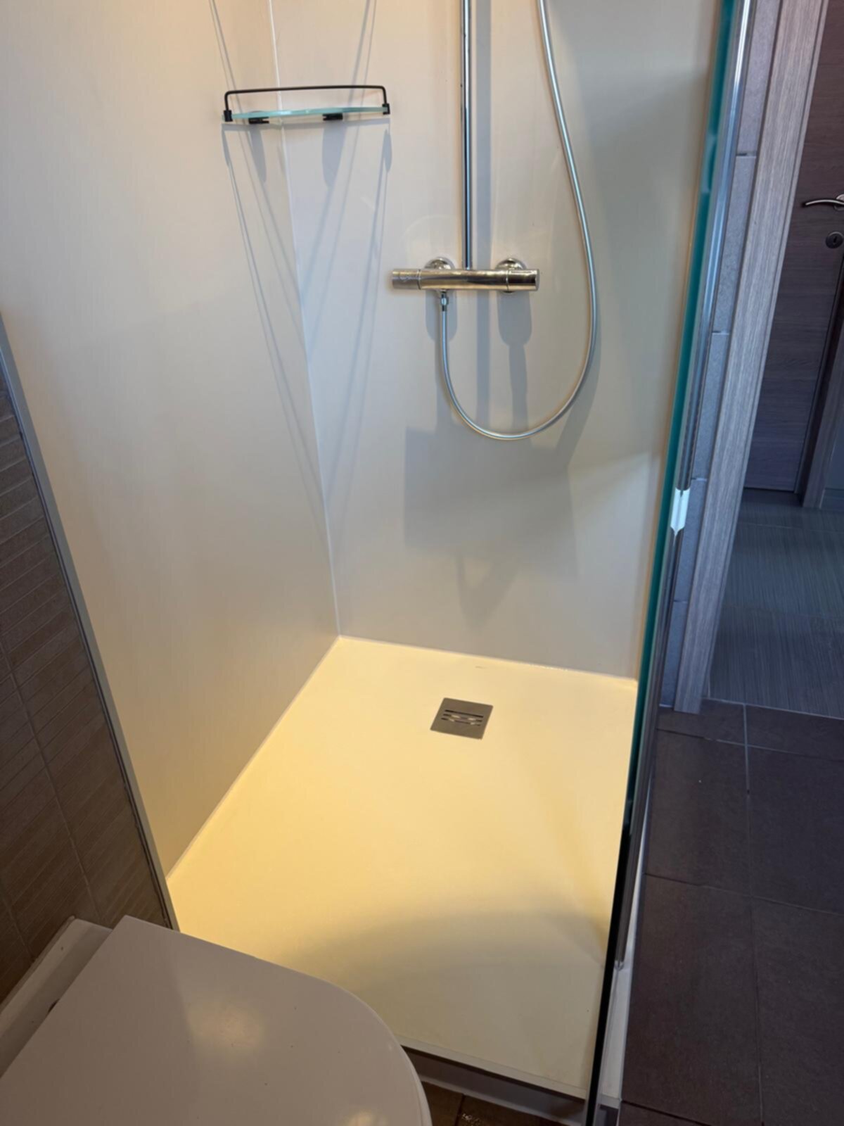 Douchecabine met witte wanden en vloer, chroom douchekraan en glasdeur
