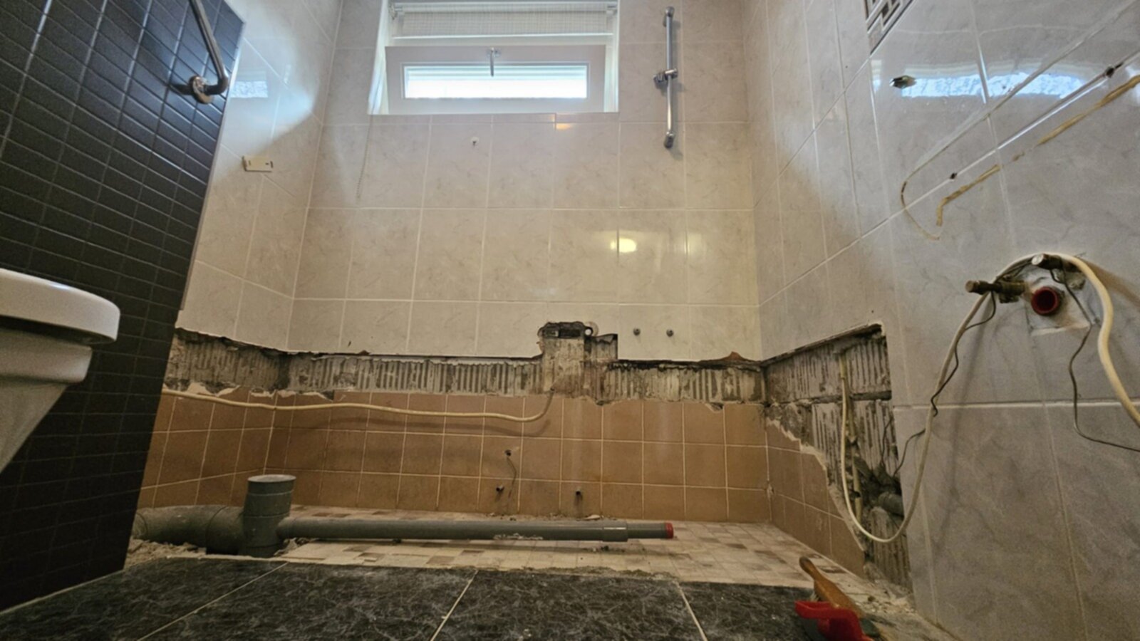Slecht onderhouden badkamer met bruine en beige tegels, toilet en zwarte marmeren vloer