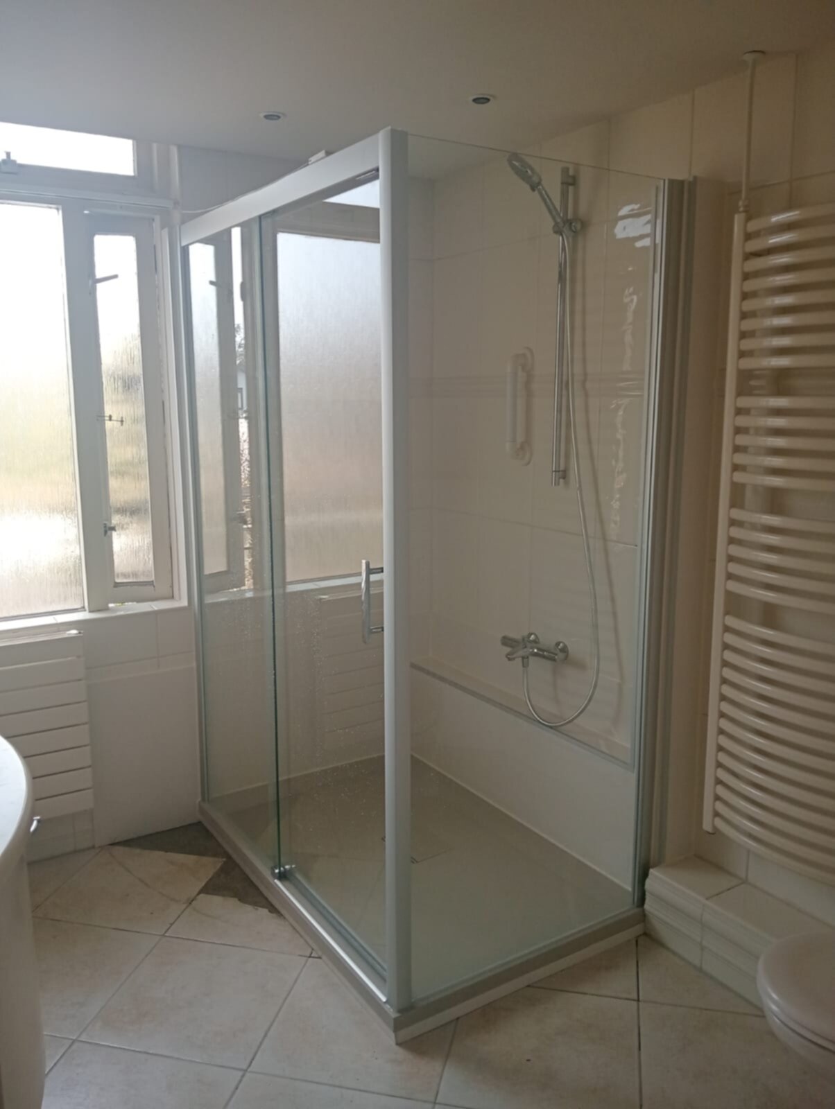 Douchecabine met glazen wand en deur, witte tegelwanden en beige vloer
