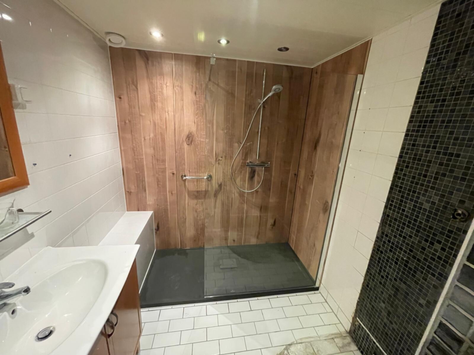 Badkamer met houten douchewand, witte tegelwanden en zwarte mozaïekvloer