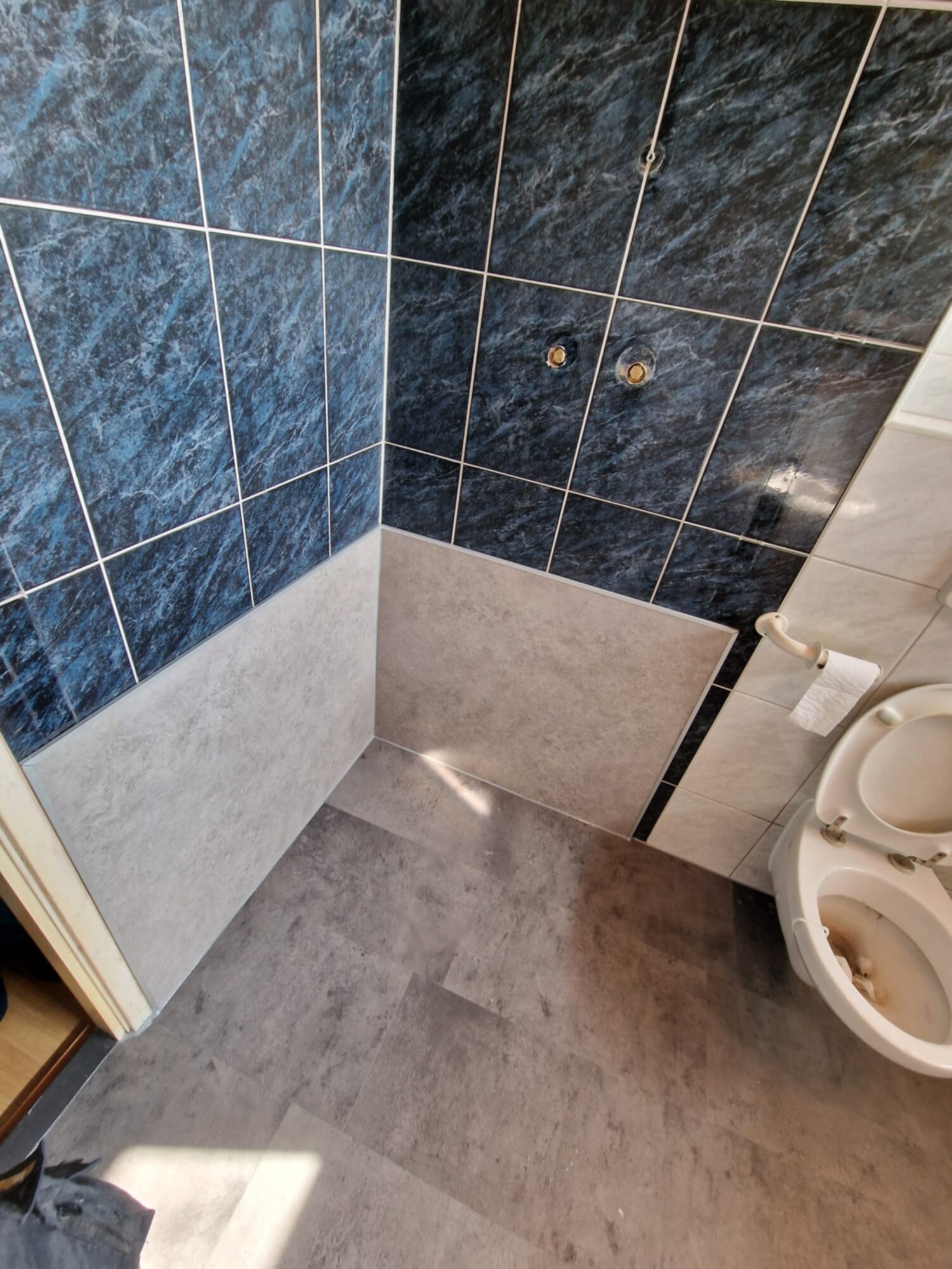 Blauw betegelde wand en grijze vloer in badkamer met toilet