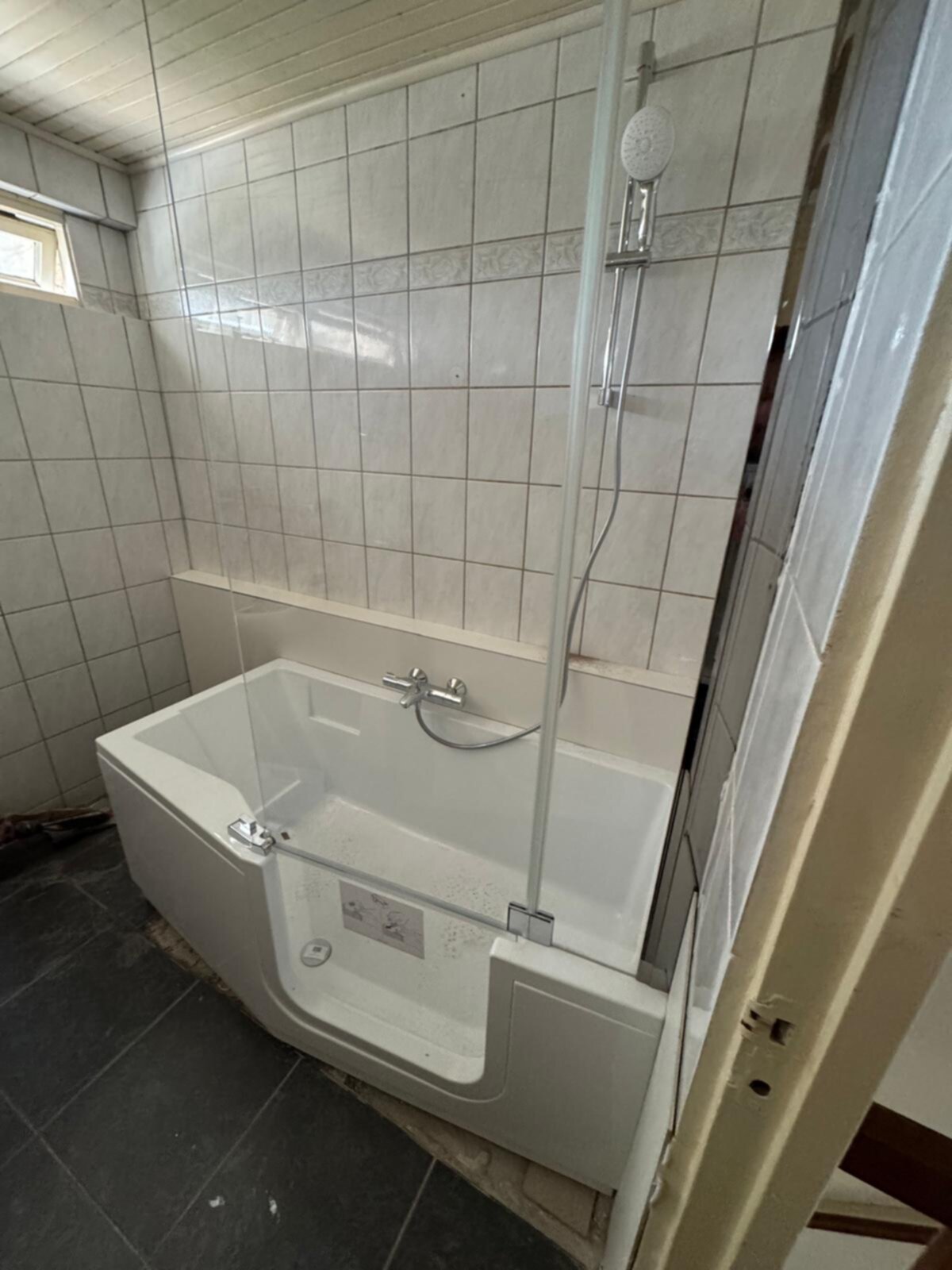 Wit bad met douche en betegelde wanden en vloer