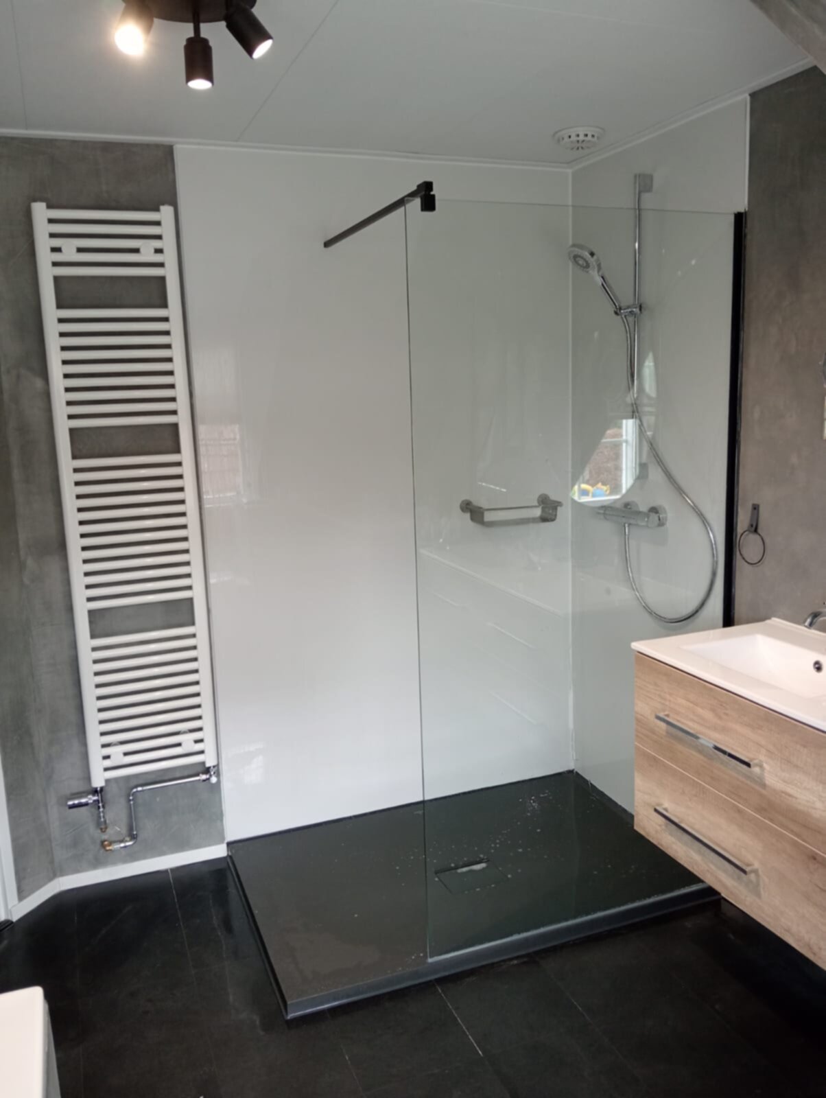 Moderne badkamer met glazen douchecabine, houten wastafel en witte radiator