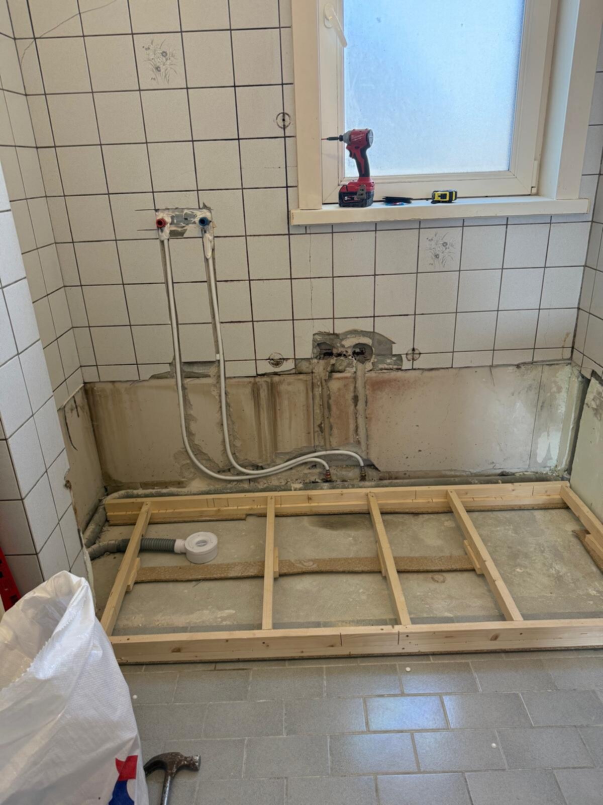 Badkamer renovatie in uitvoering, betegelde muren en vloer, houten ondergrond voor nieuwe vloer
