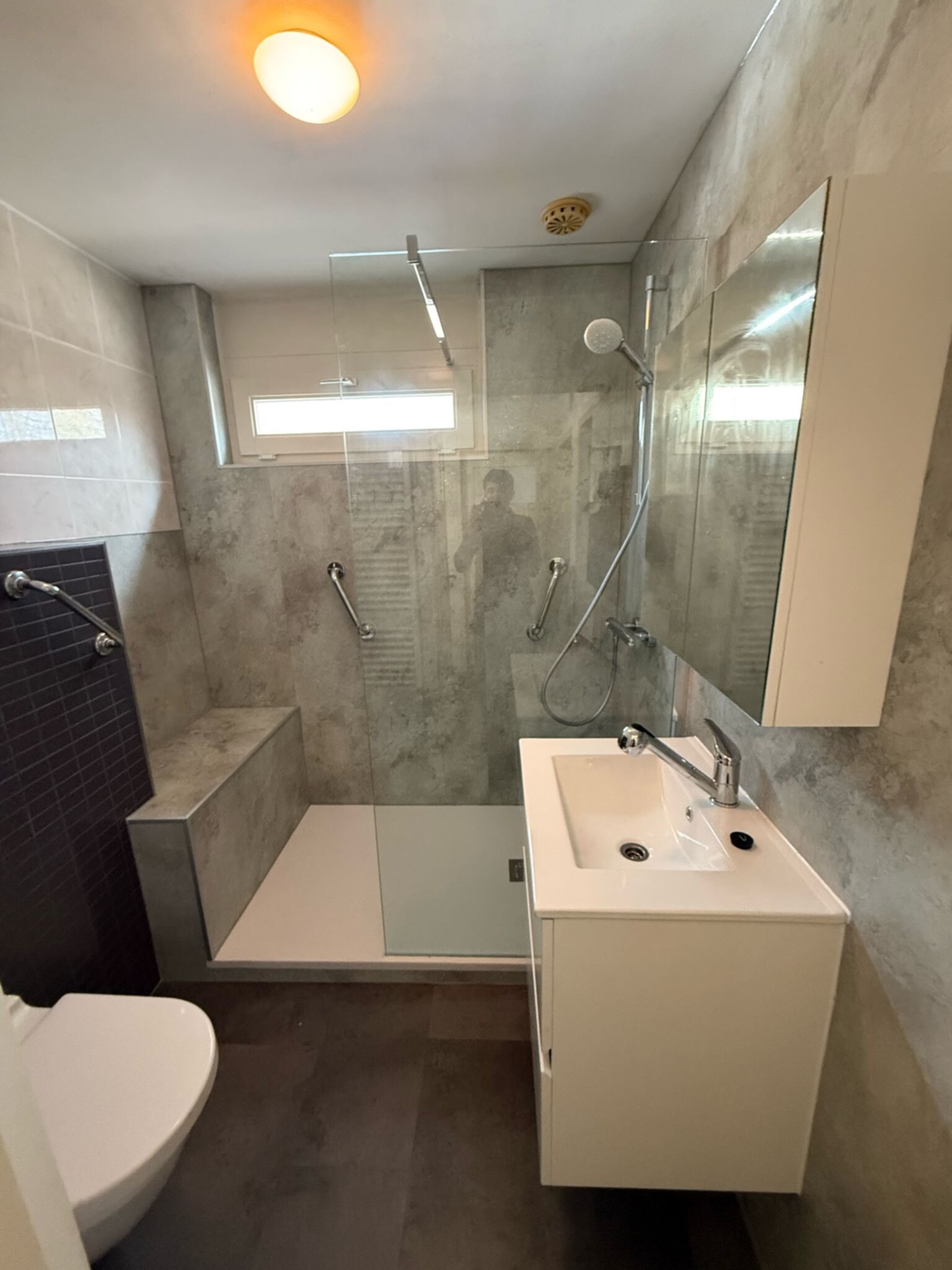 Moderne badkamer met grijze tegels, witte wasbak en toilet, en een glazen douchecabine.