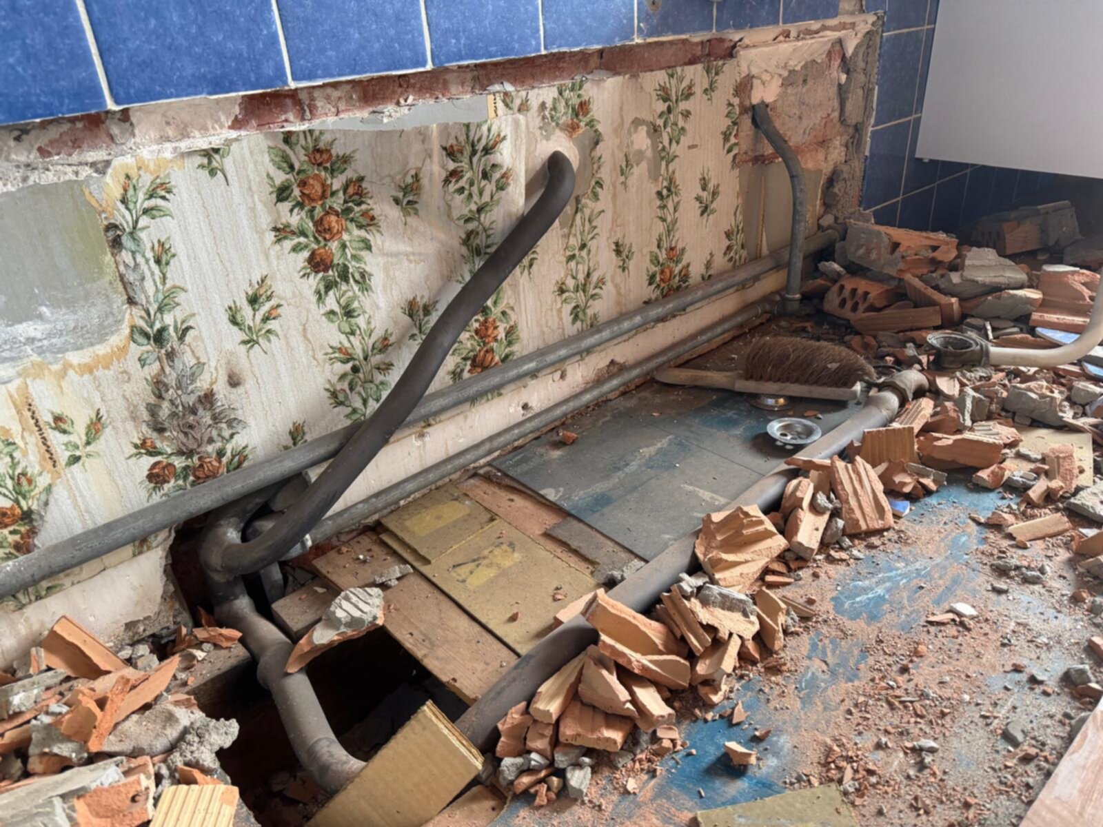 Sloopwerkzaamheden in badkamer met bloemensierpapier en kapotte tegels