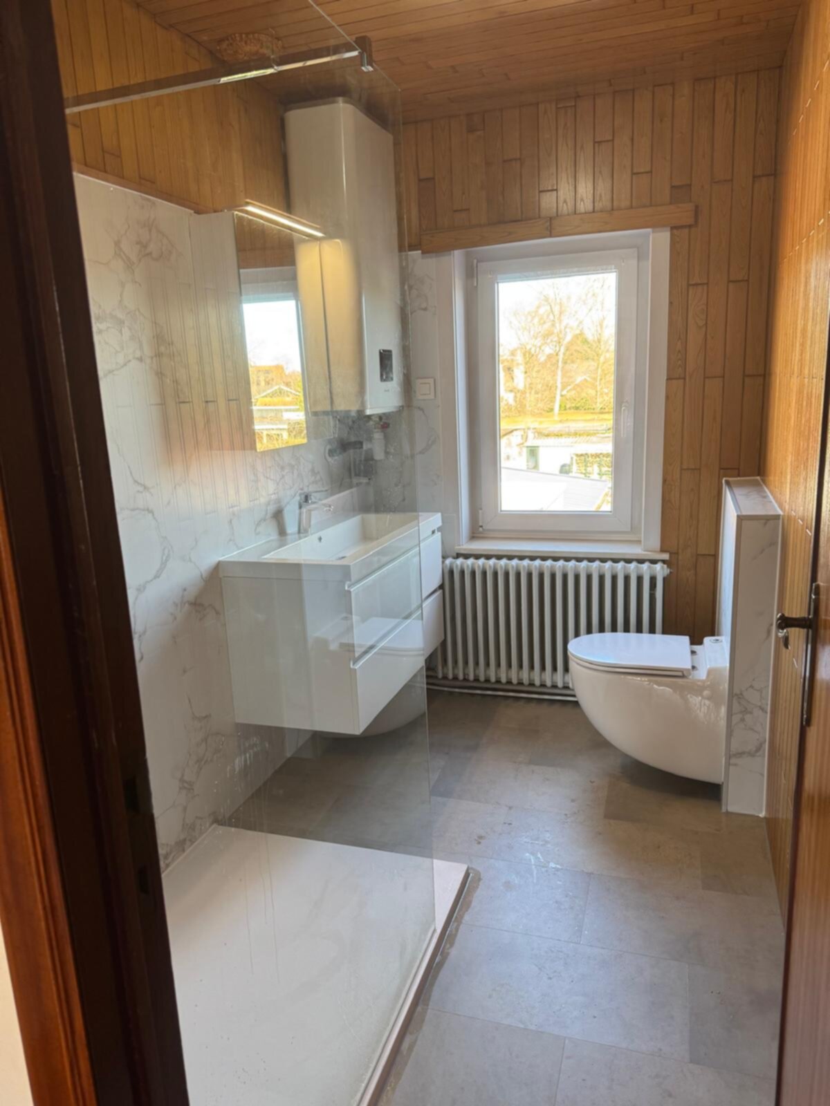 Badkamer met houten wandpanelen, witte wastafel en toilet, marmeren tegelwerk