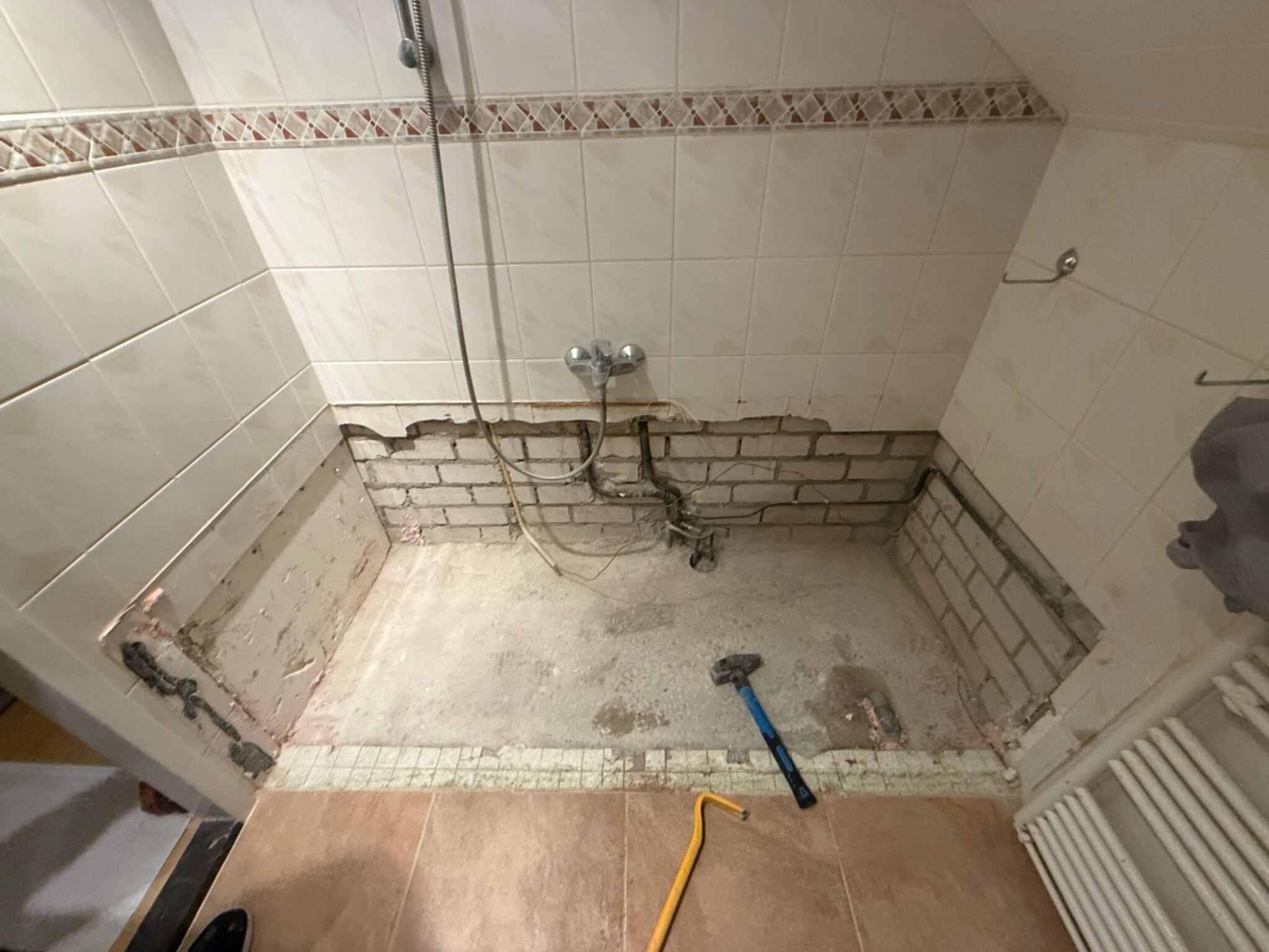 Slechte staat badkamer met kapotte tegelwerk en gereedschap op de grond