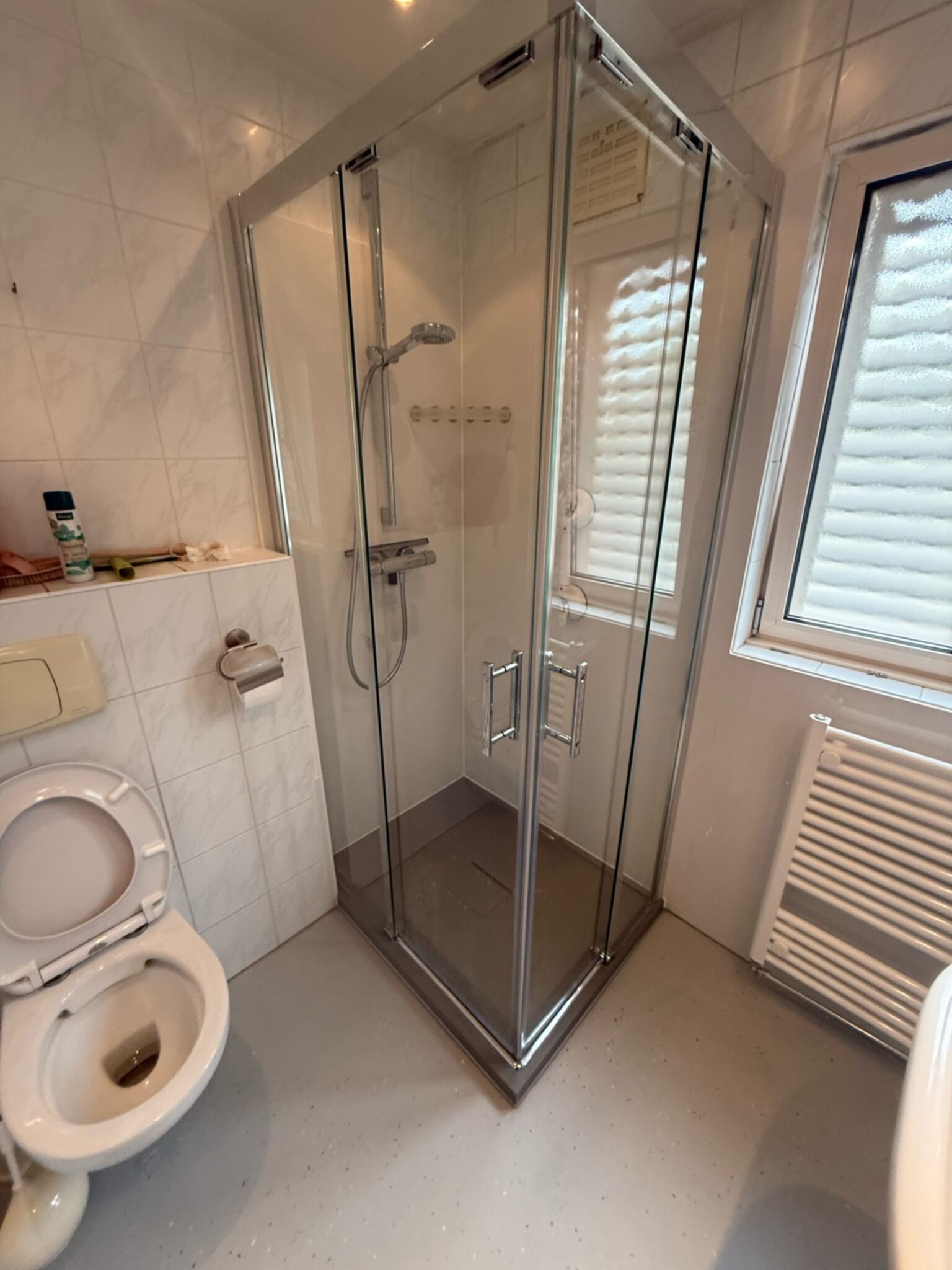 Badkamer met witte tegelwanden en grijs toilet en douche