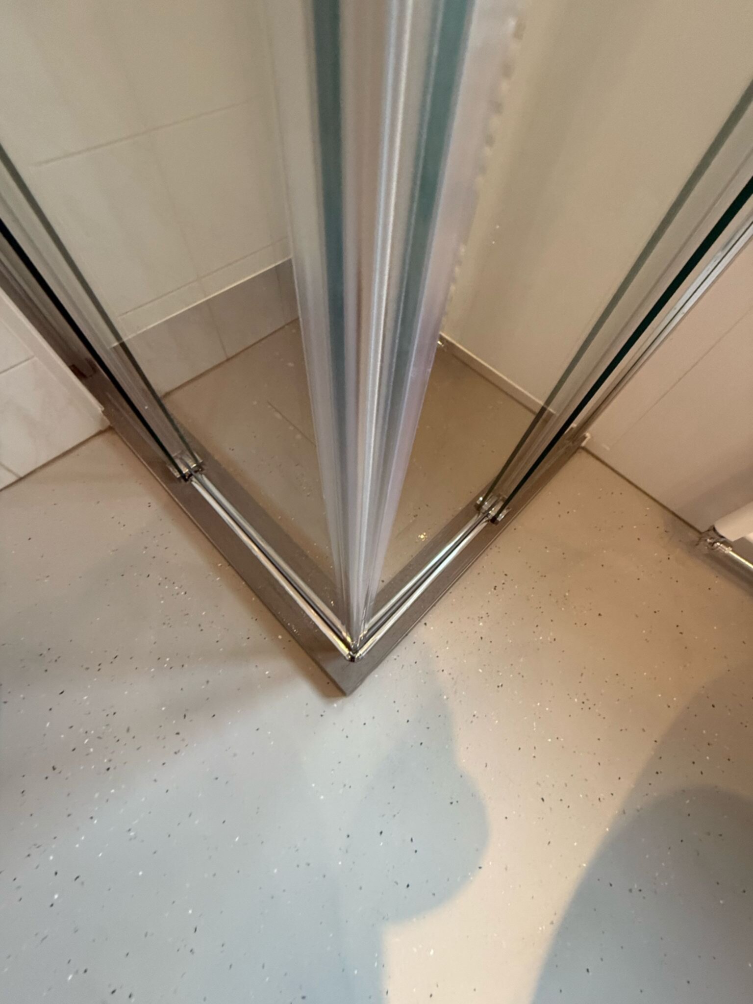Douchehoek met glazen schuifdeur en witte tegelwanden en -vloer met spikkels