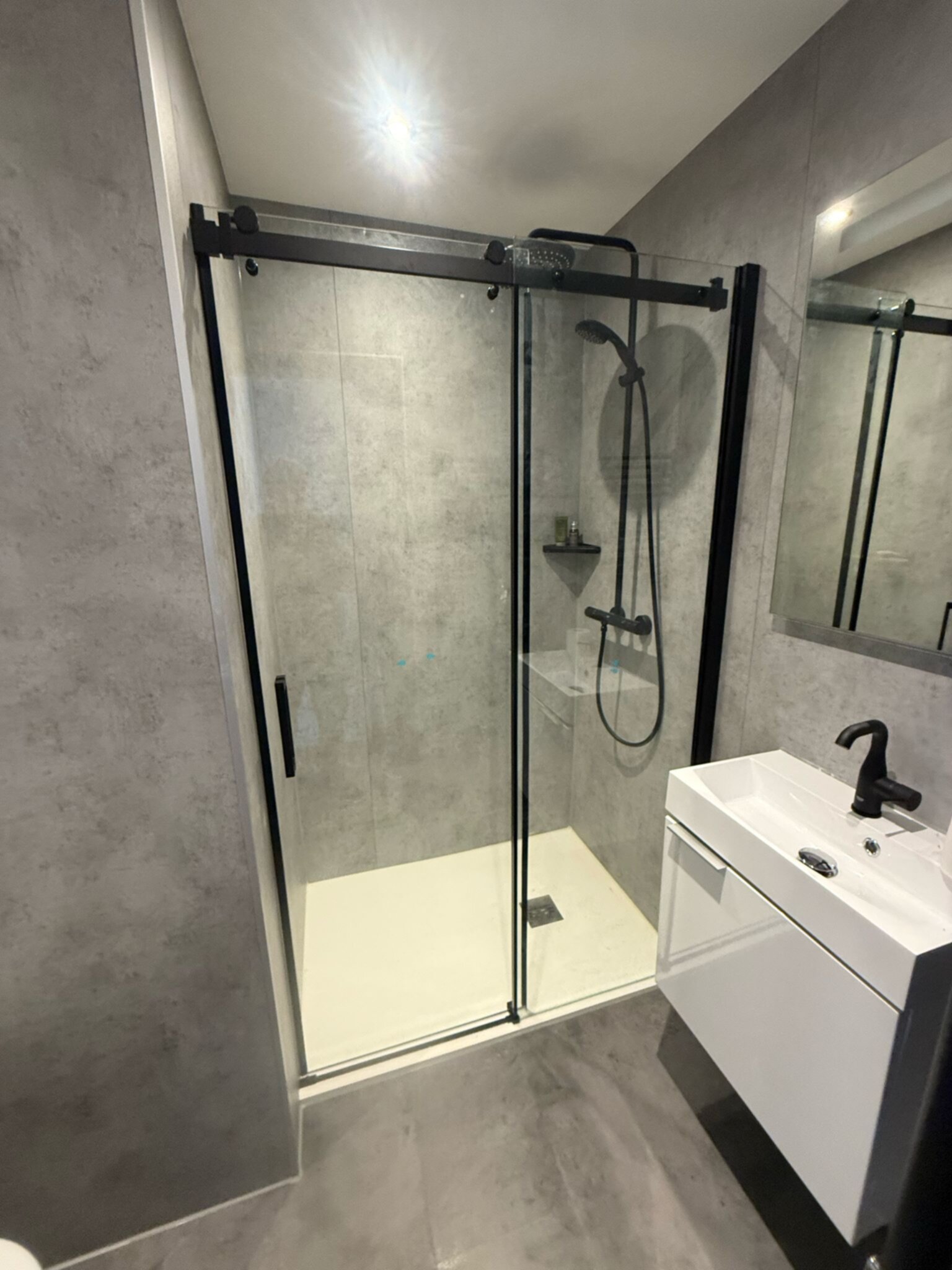 Moderne badkamer met grijze tegelwanden, glazen douchecabine en witte wasbak