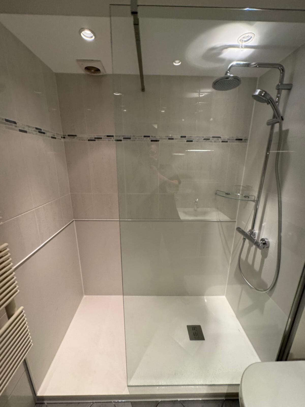 Douchecabine met glazen wand en deur, witte en grijze tegels, chroom douchekraan.