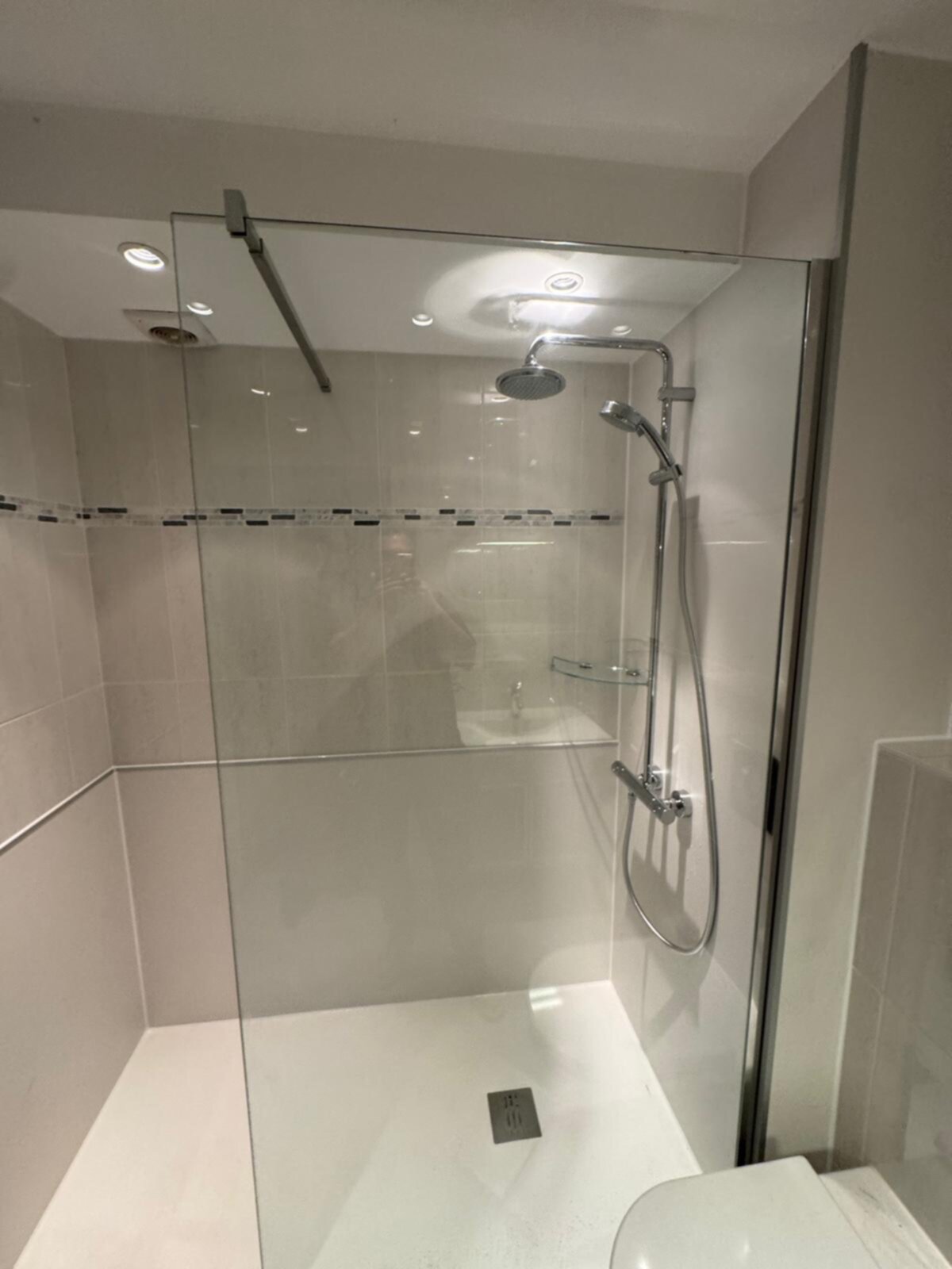 Douchecabine met glazen wand en deur, witte tegelvloer en beige wandtegels
